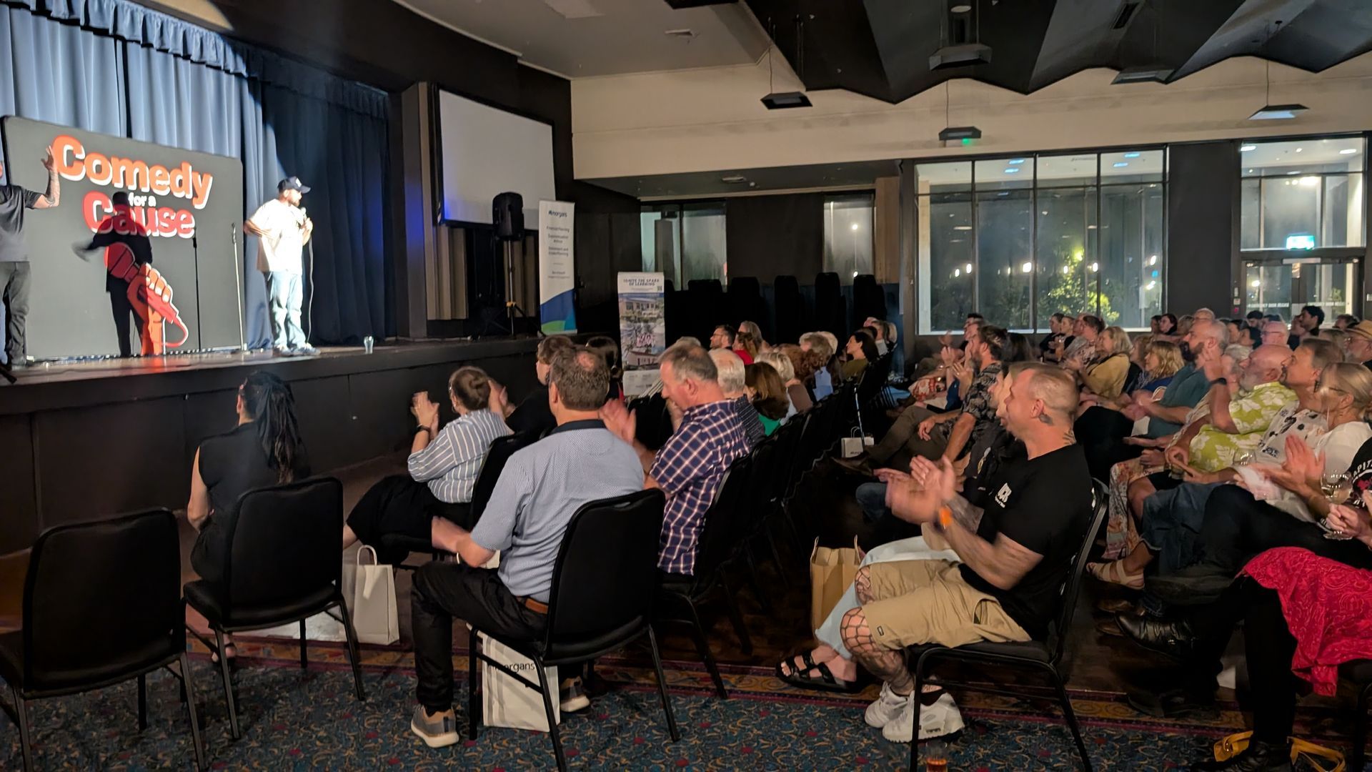 A crowd of people are sitting in chairs in front of a stage watching a comedy show.