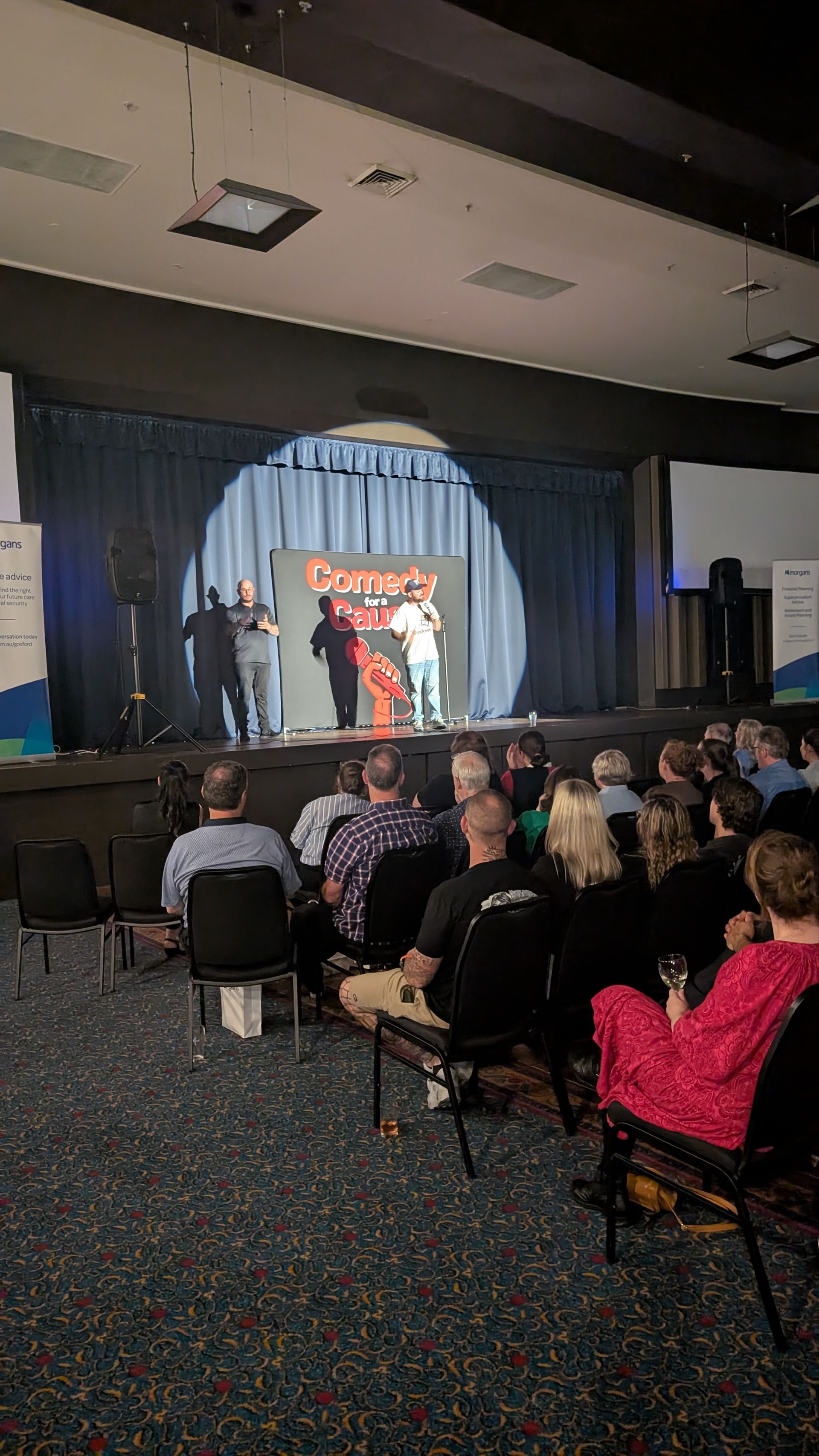 A group of people are sitting in chairs in front of a stage watching a comedy show.