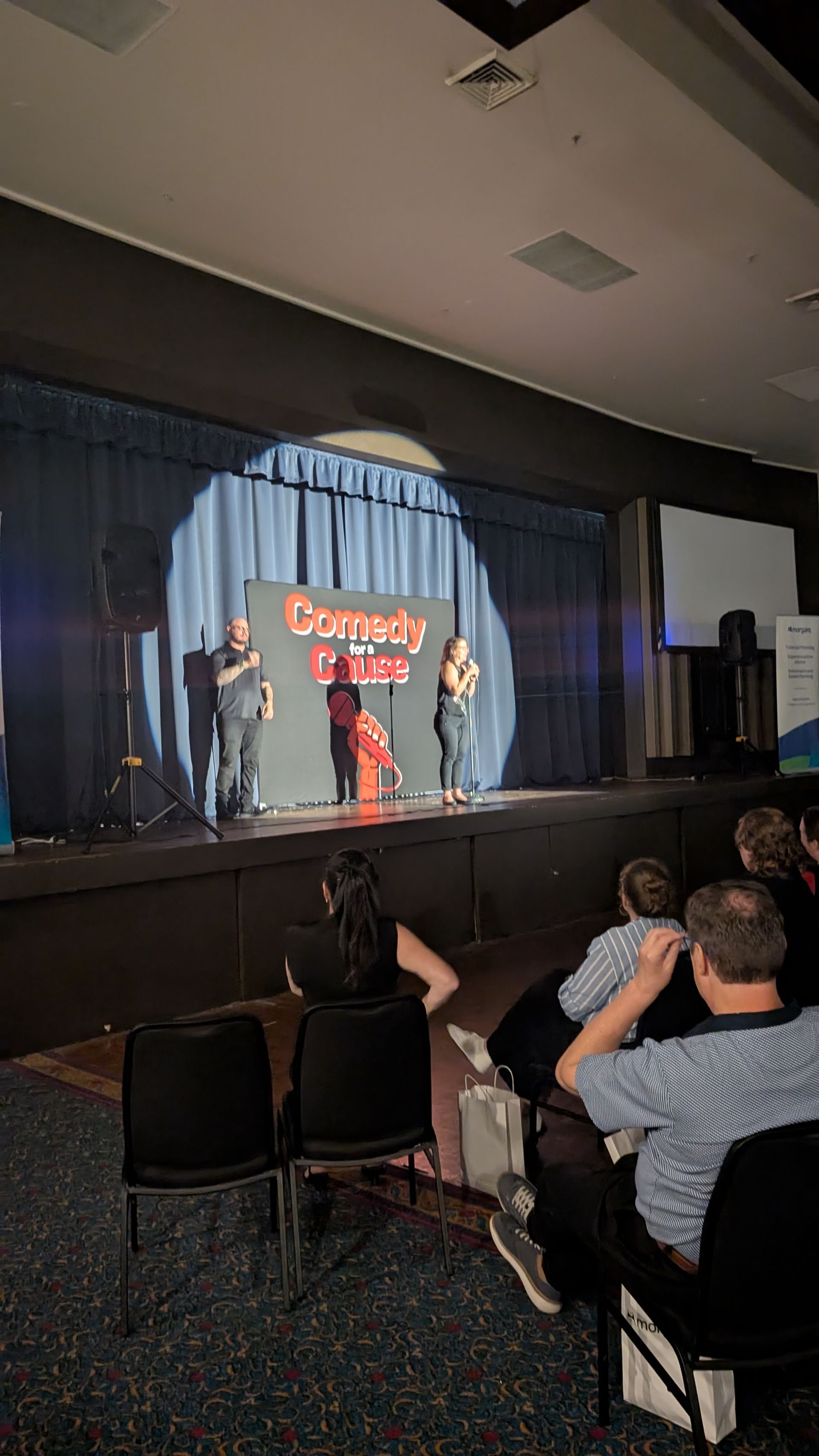 A group of people are sitting in chairs in front of a stage watching a comedy show.
