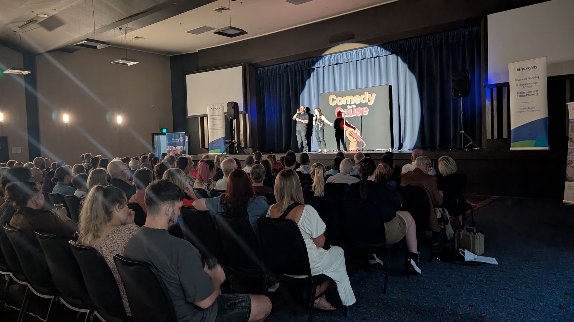 A crowd of people are sitting in front of a stage at a comedy show.