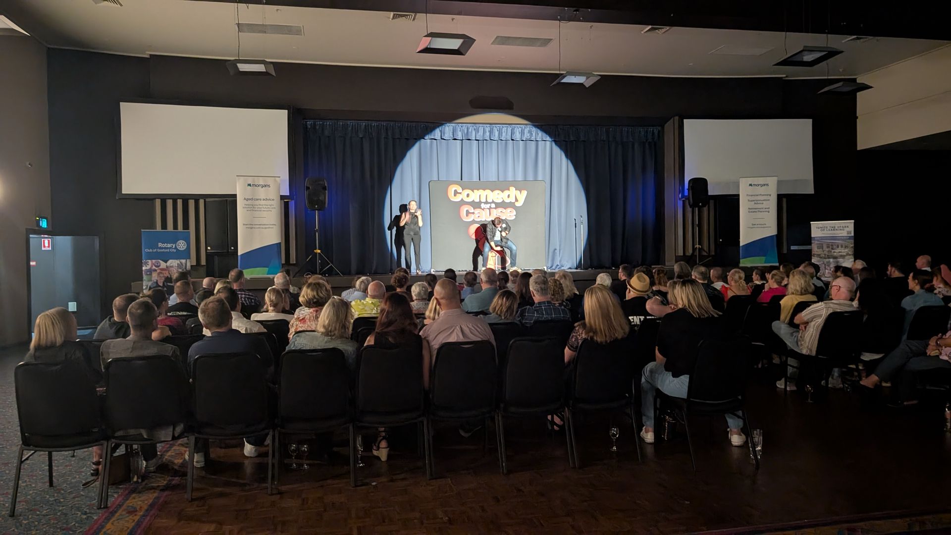 A large group of people are sitting in chairs in front of a stage.