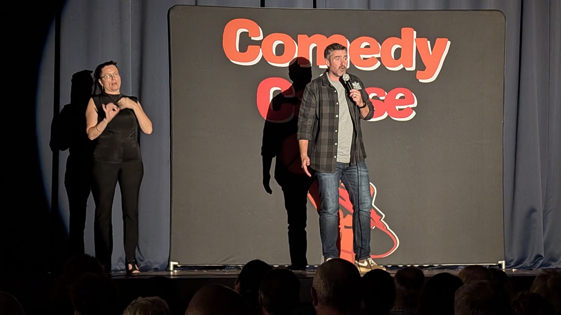 A man stands on a stage in front of a sign that says comedy for a cause