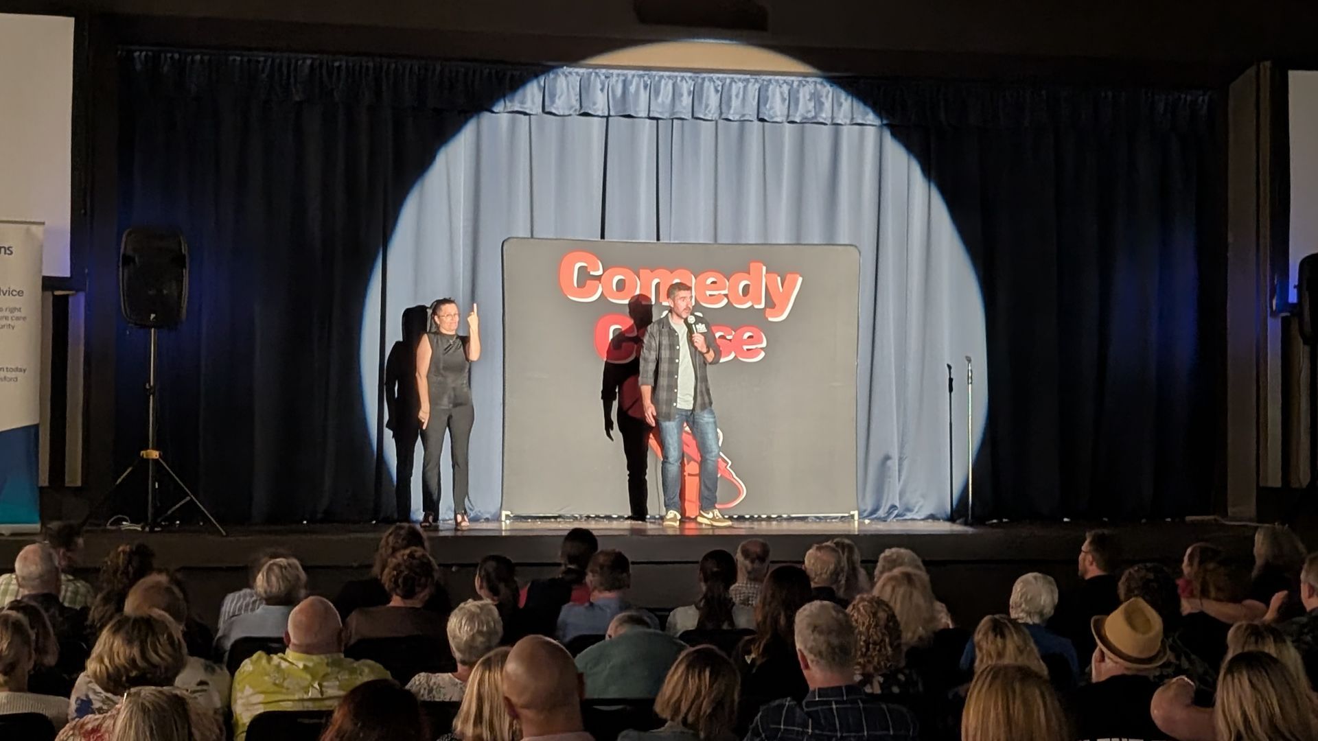 A group of people are sitting in front of a stage watching a comedy show.
