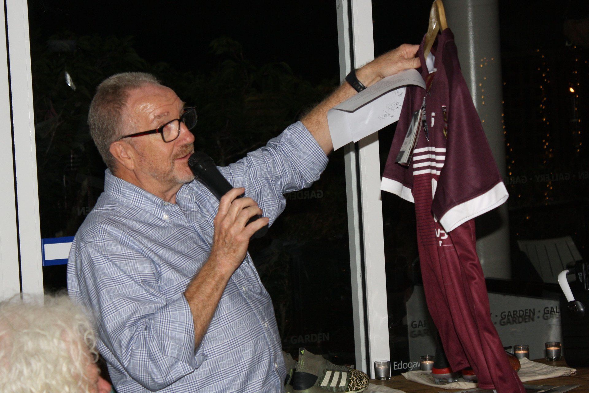 A man is holding a microphone and pointing at a shirt hanging on a hanger.