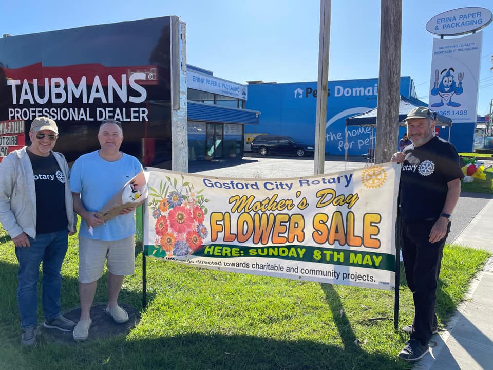 Three men are standing in front of a sign that says flower sale