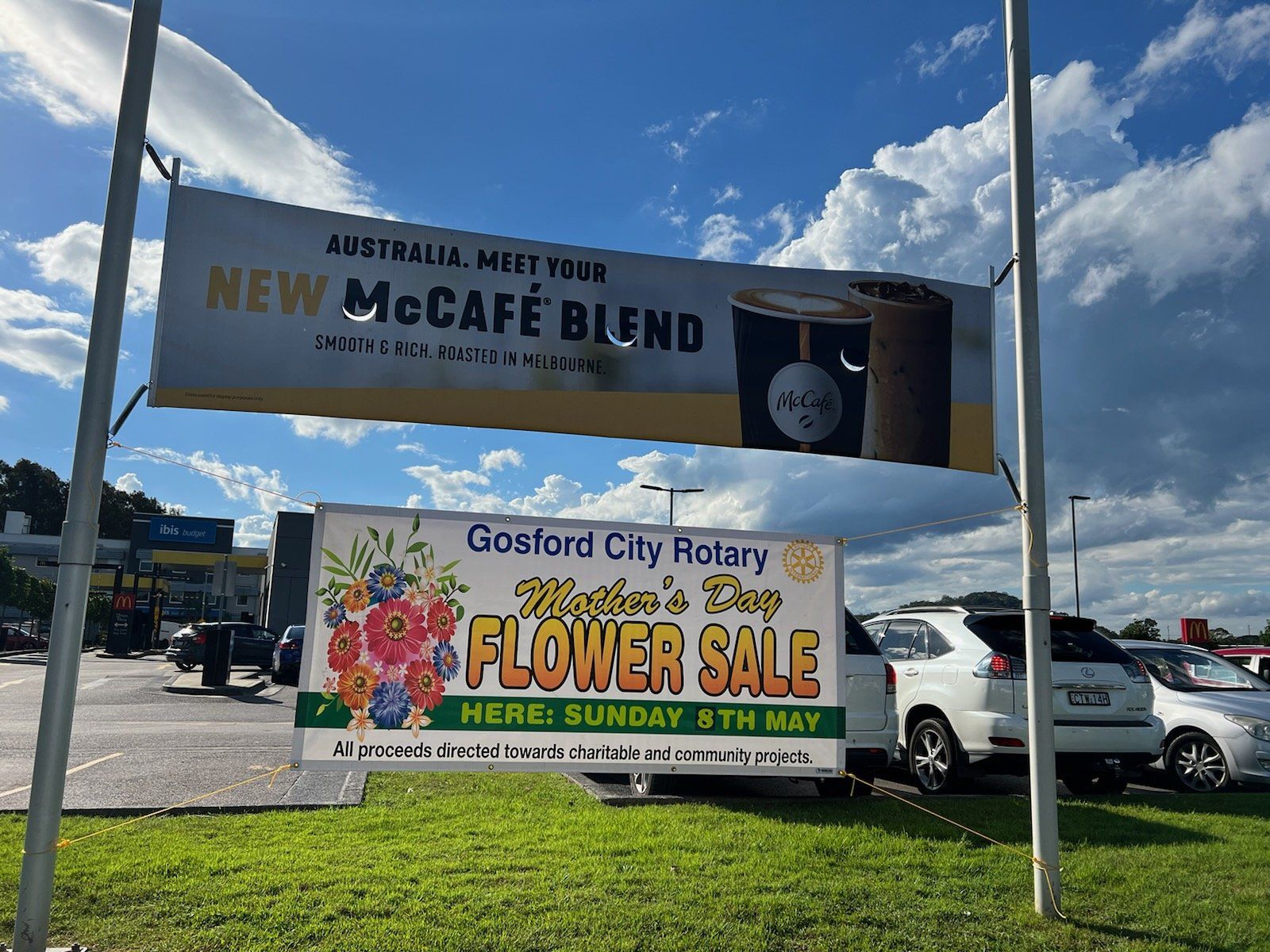 A sign for a flower sale is hanging from a pole in a parking lot.