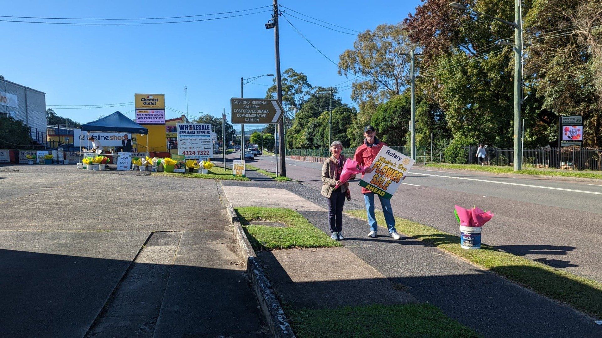 A couple of people standing on a sidewalk next to a road.