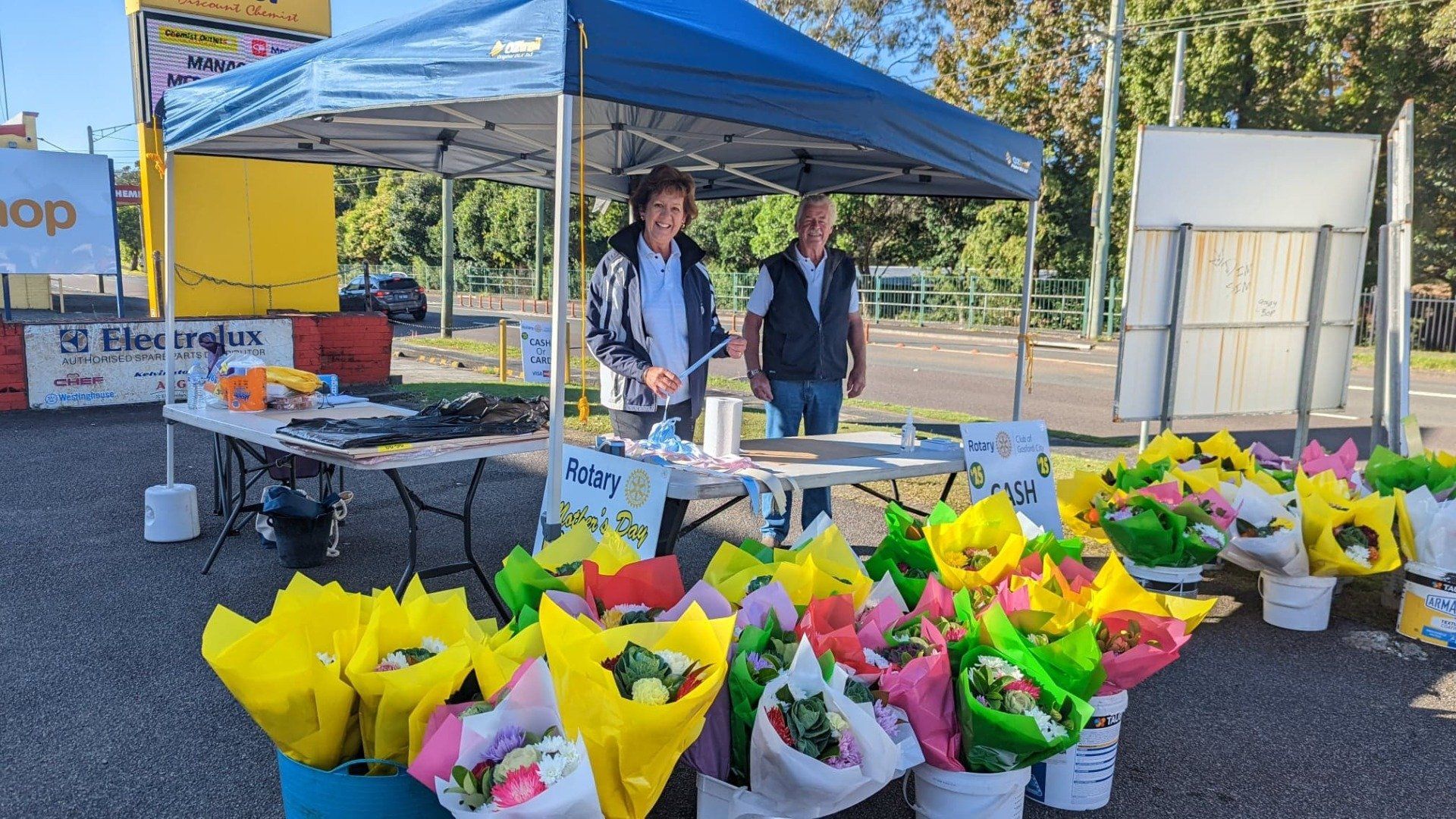 Two men are standing in front of a table filled with lots of flowers.
