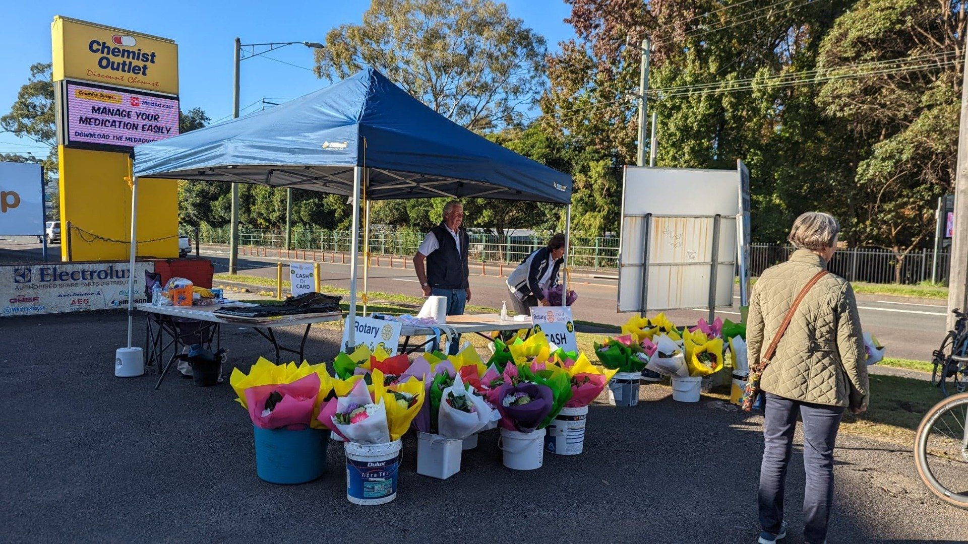 A man is selling flowers under a tent in a parking lot.