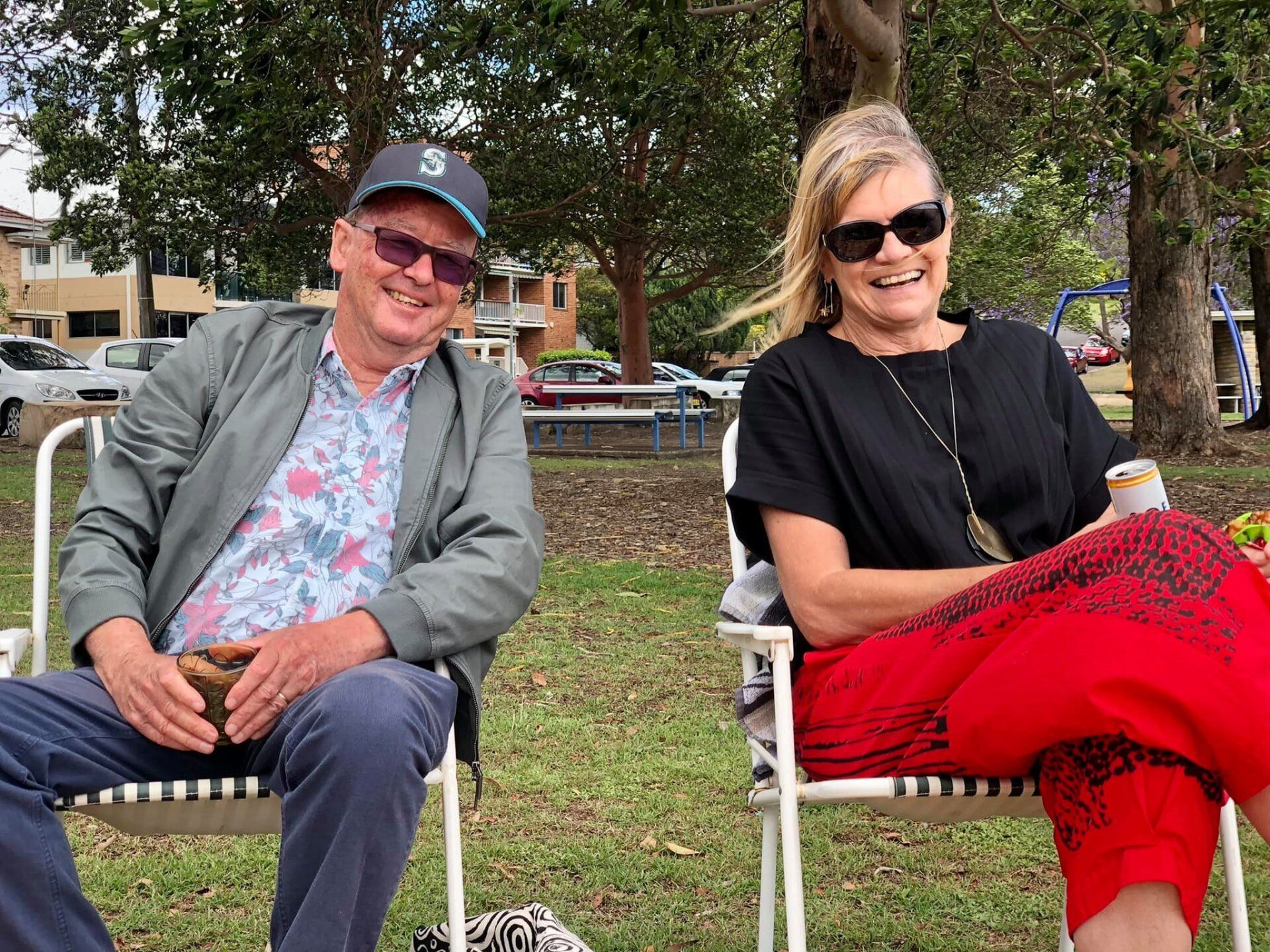 A man and a woman are sitting in chairs in a park.