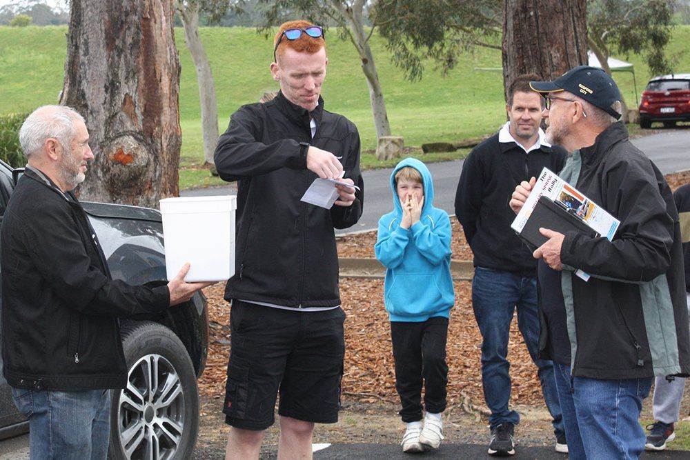 A group of men are standing in front of a car talking to each other.