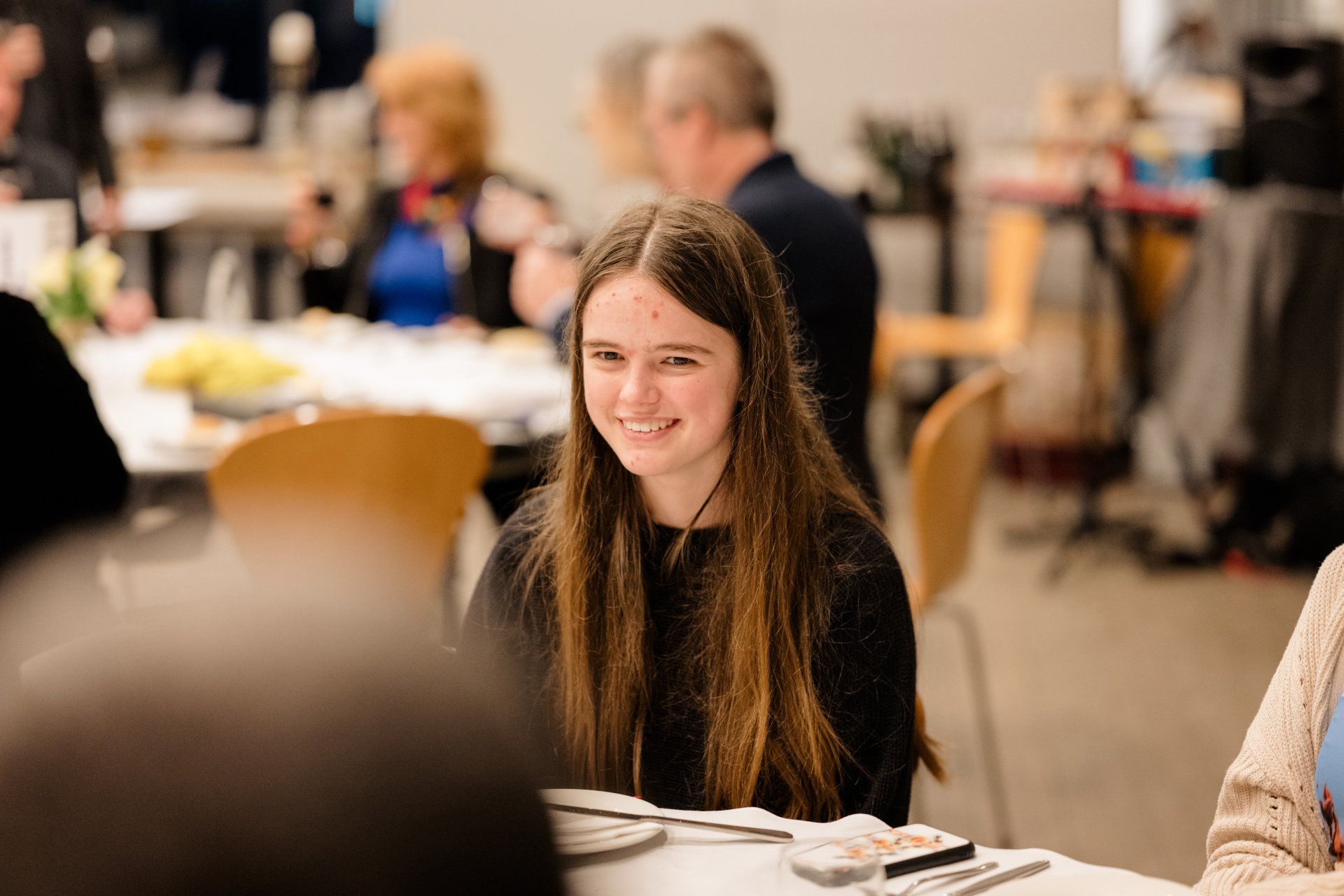 A young girl is sitting at a table in a restaurant with other people.