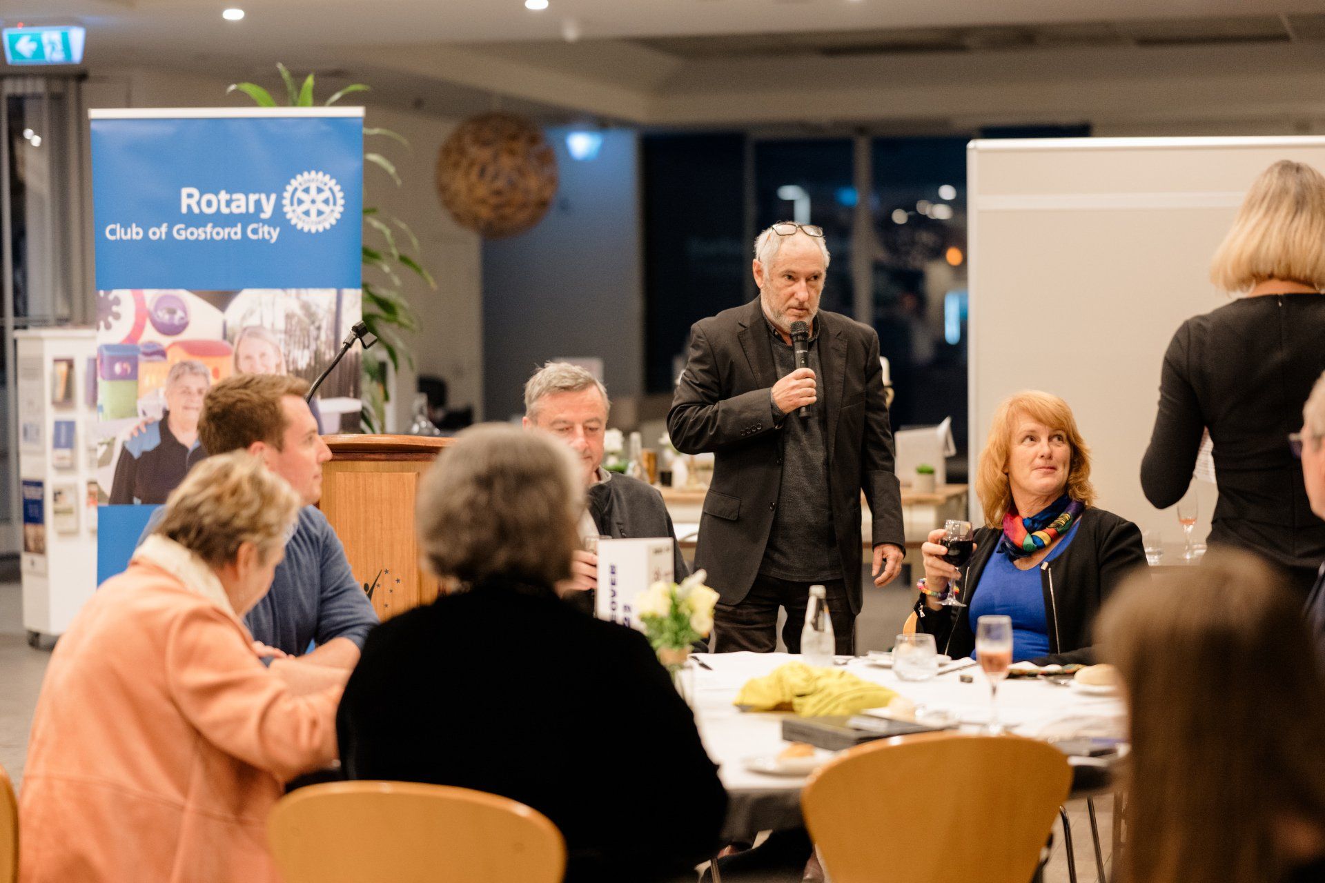 A man is standing in front of a group of people sitting at tables.