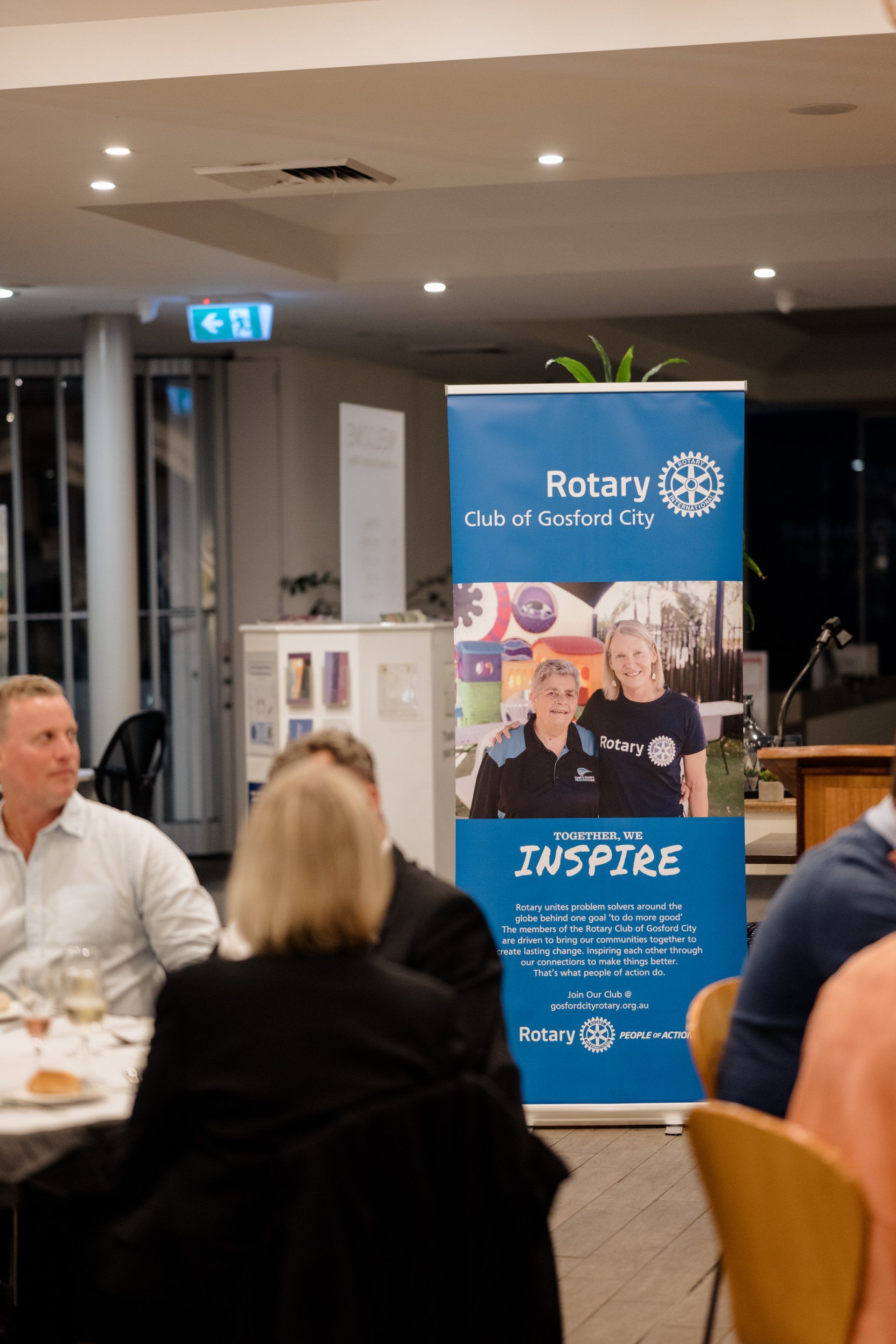 A group of people are sitting at a table in front of a sign that says rotary