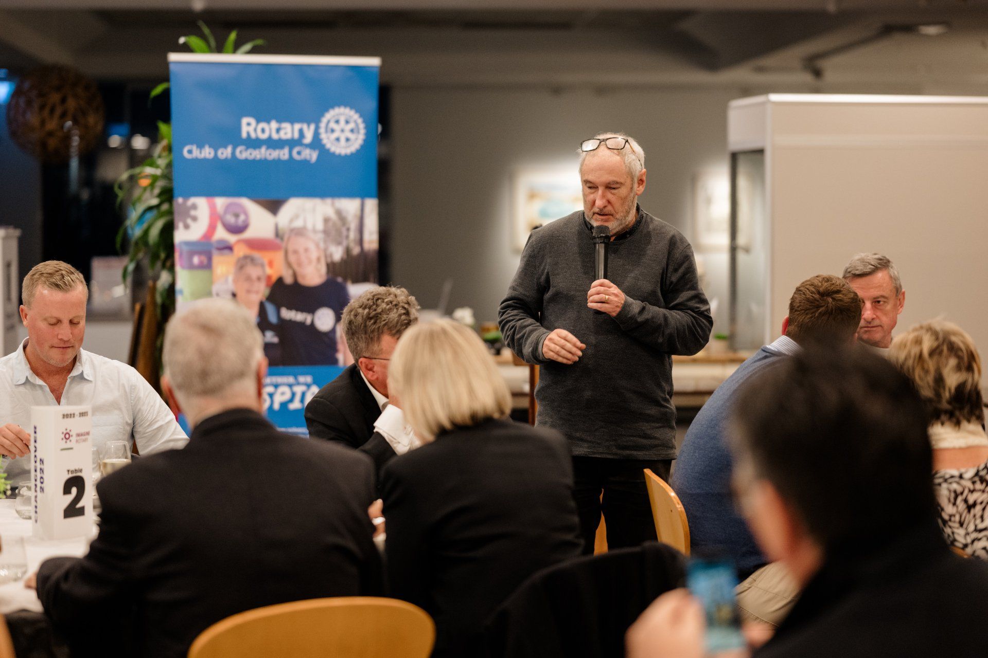 A man is standing in front of a microphone talking to a group of people.