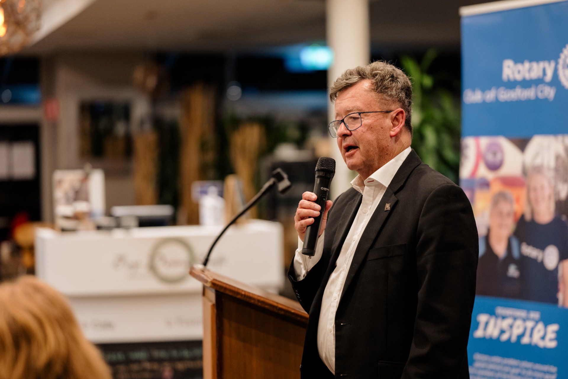 A man in a suit is standing at a podium holding a microphone.