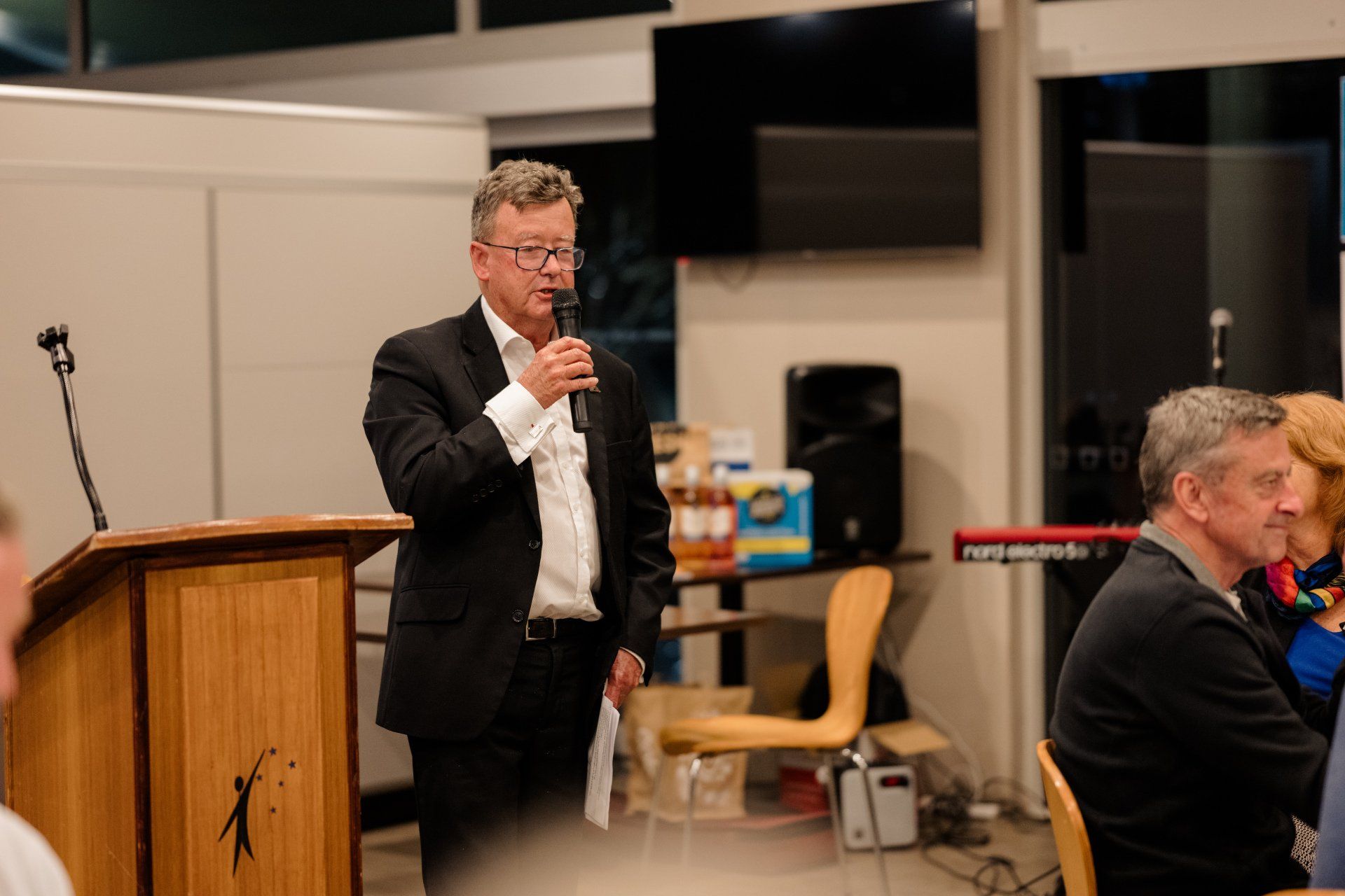 A man in a suit is standing at a podium talking into a microphone.