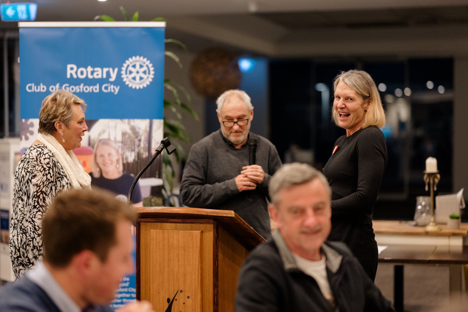 A group of people are standing around a podium in front of a sign that says rotary club of oxford city.