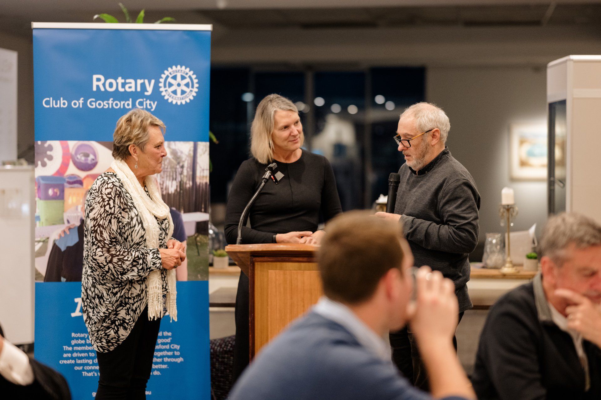 A group of people are standing around a podium in front of a rotary sign.