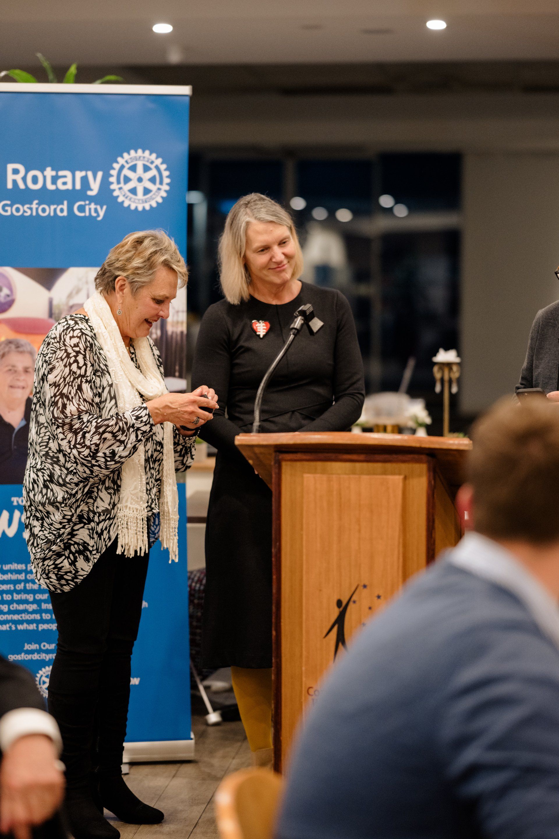 Two women are standing at a podium in front of a rotary sign.