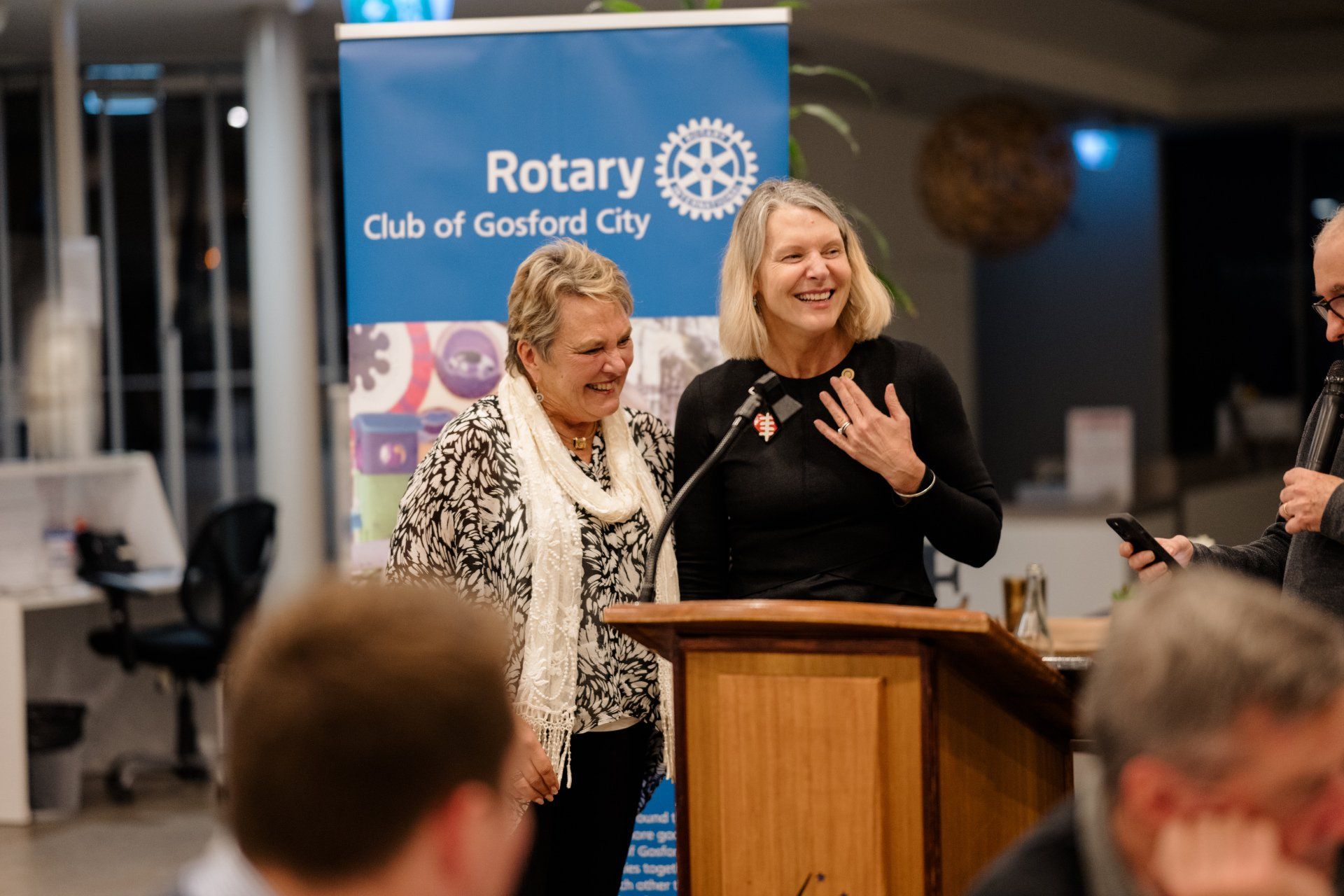 Two women are standing at a podium in front of a rotary sign.