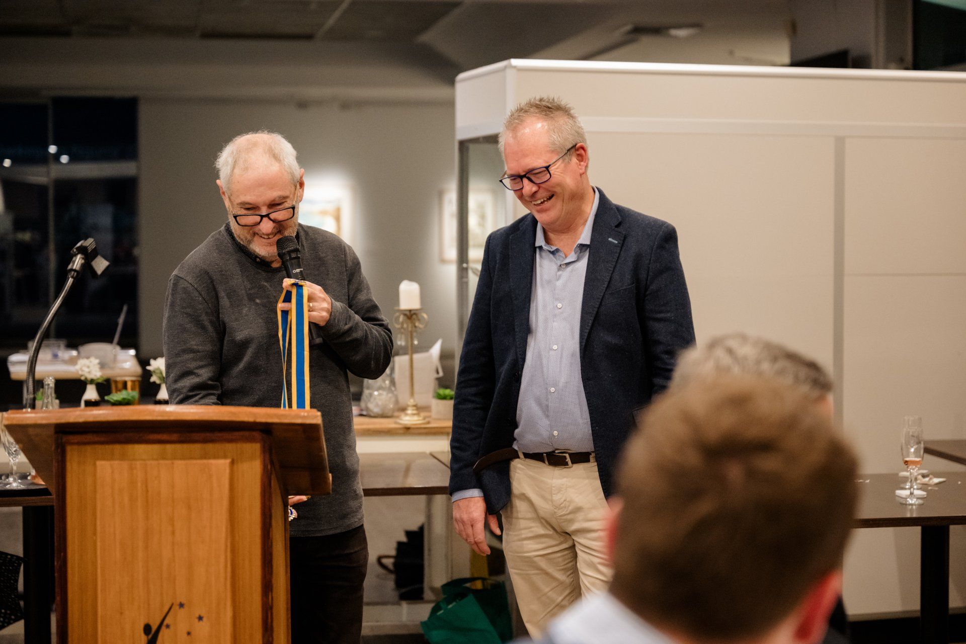 Two men are standing at a podium talking into microphones.