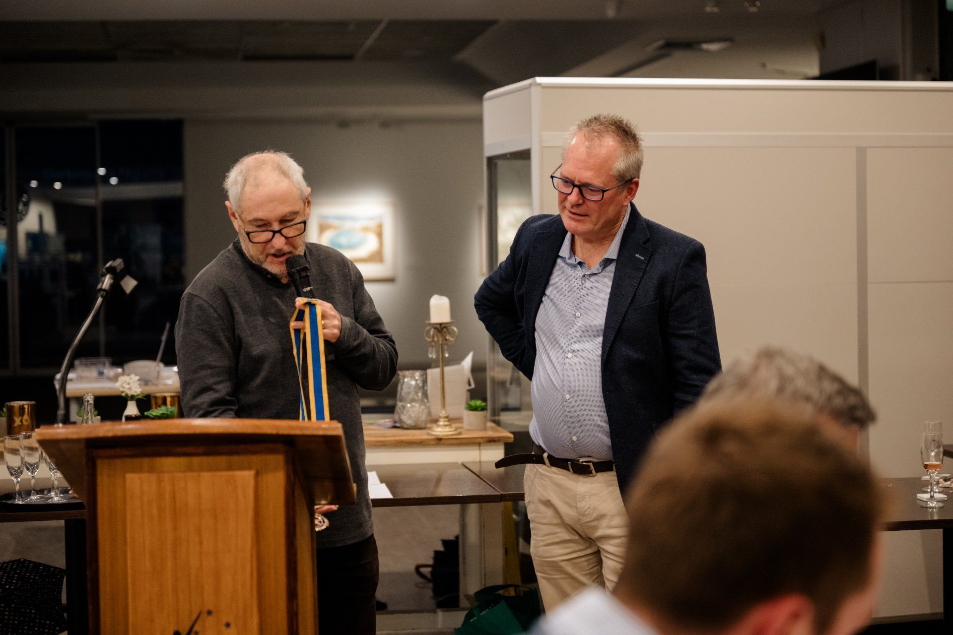 Two men are standing at a podium talking into a microphone.