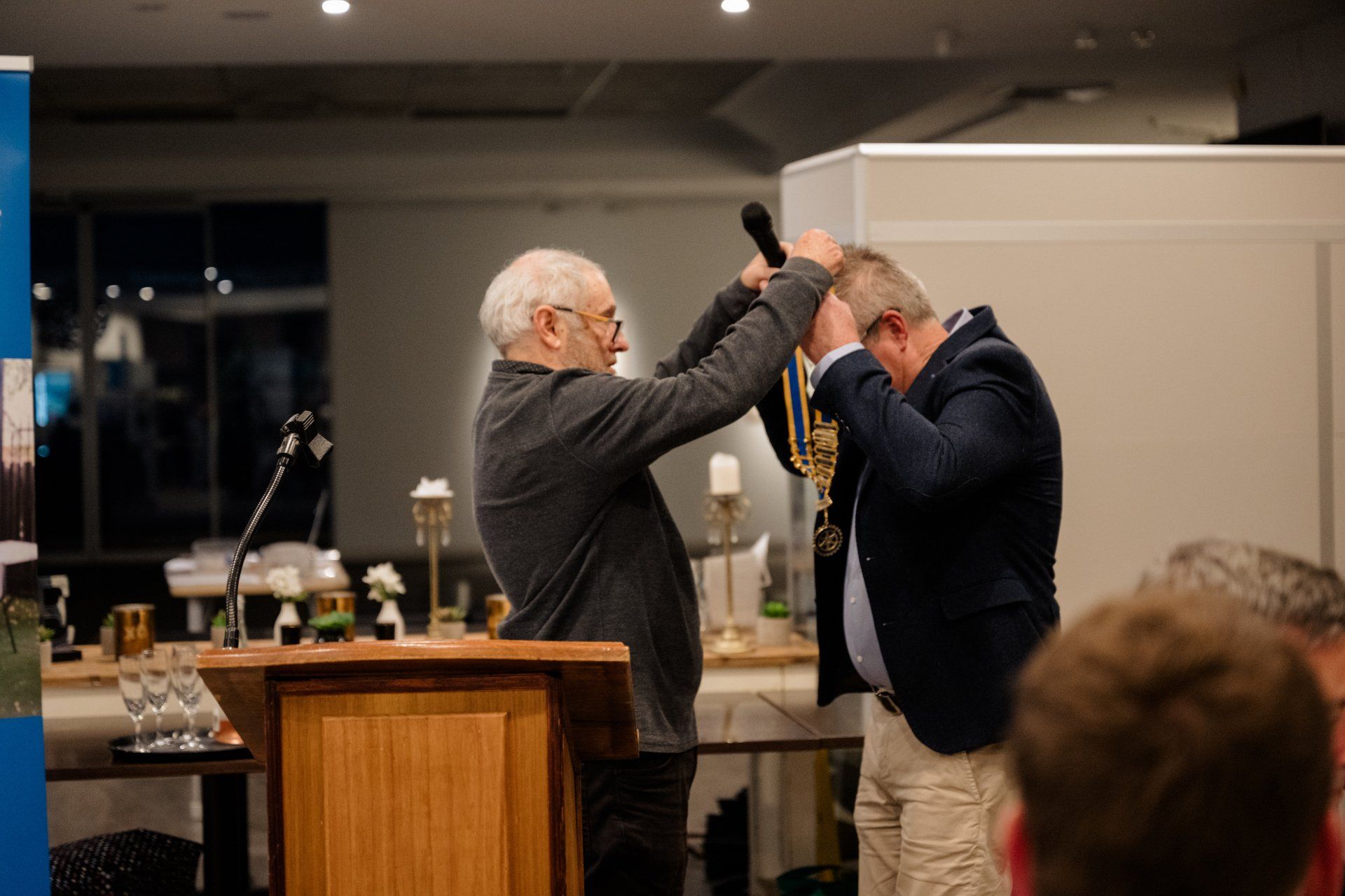 A man is putting a medal on another man 's head at a podium.