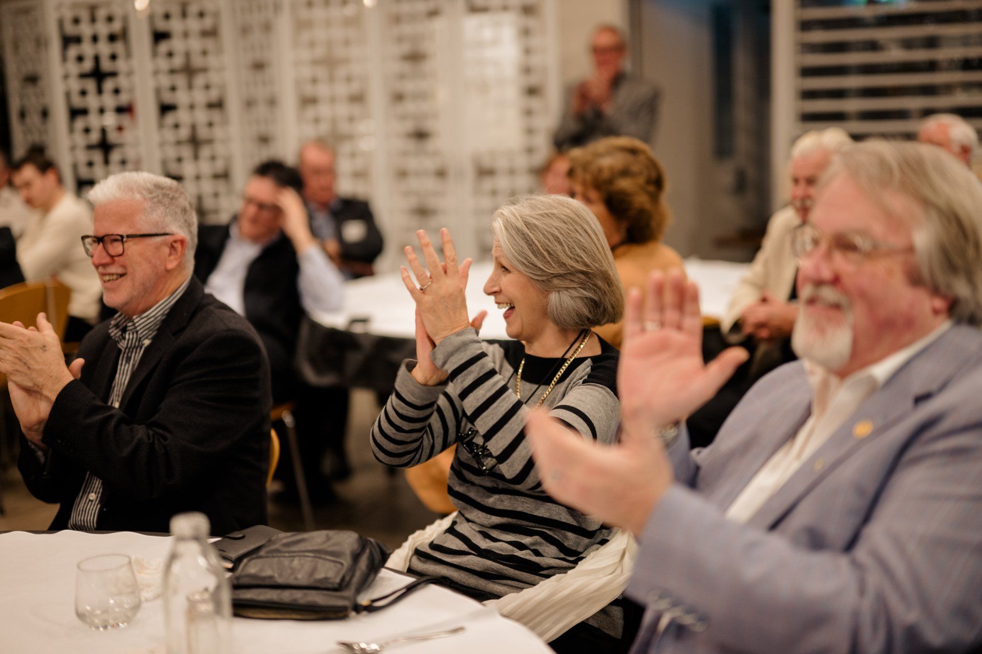 A group of people are sitting at a table clapping their hands.
