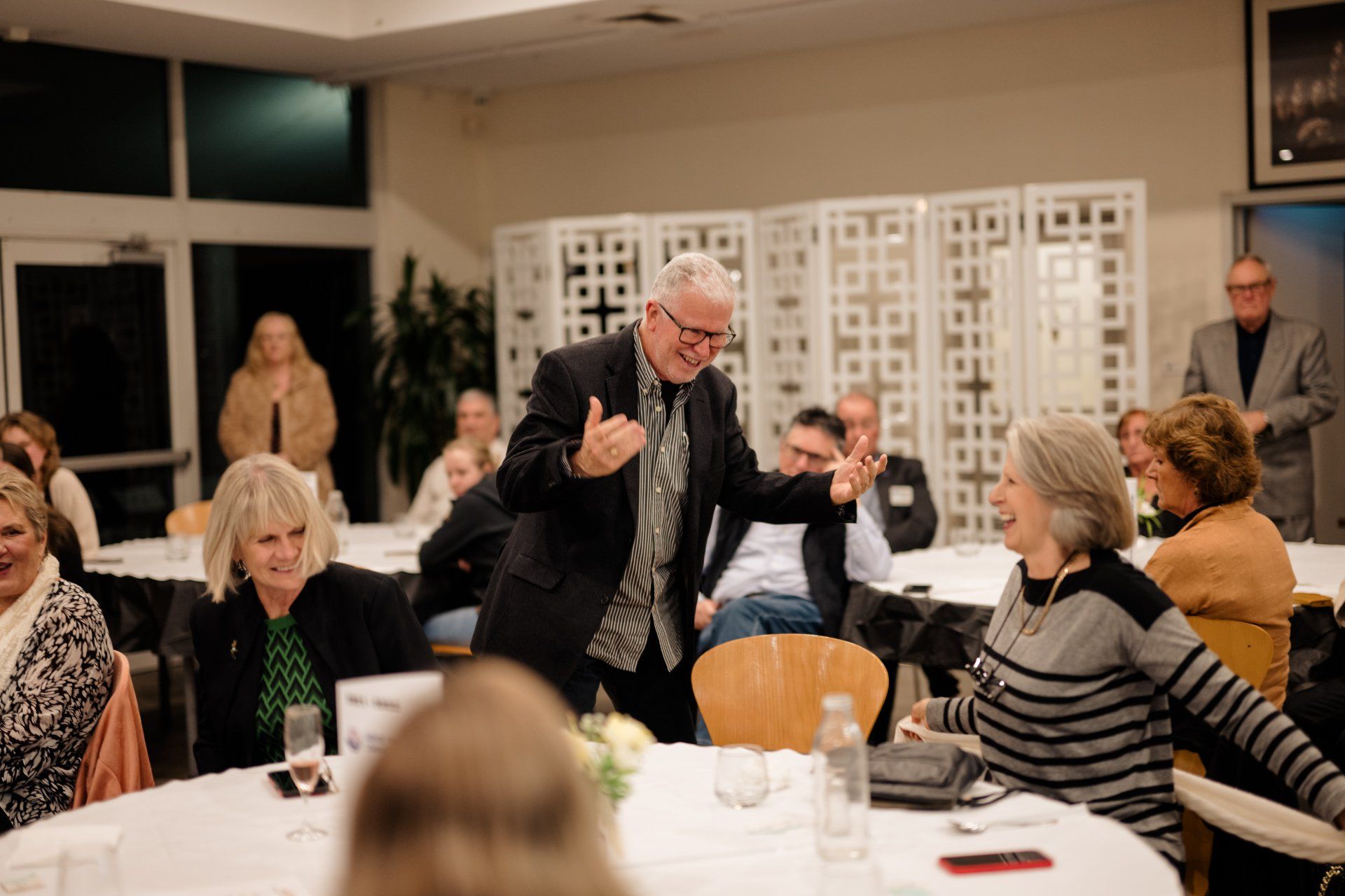 A man is standing in front of a group of people at a table.