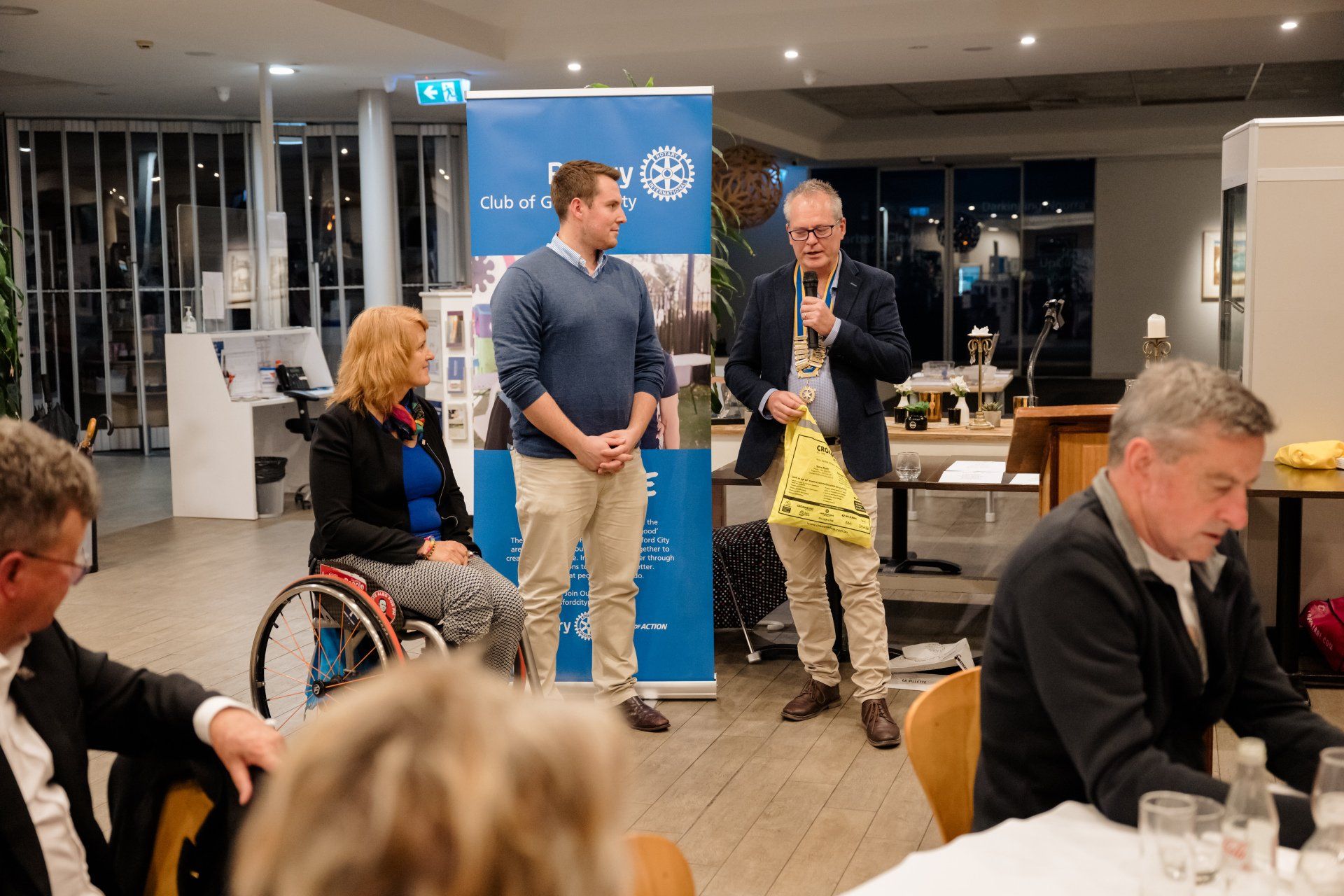A woman in a wheelchair is sitting at a table with other people at a conference.