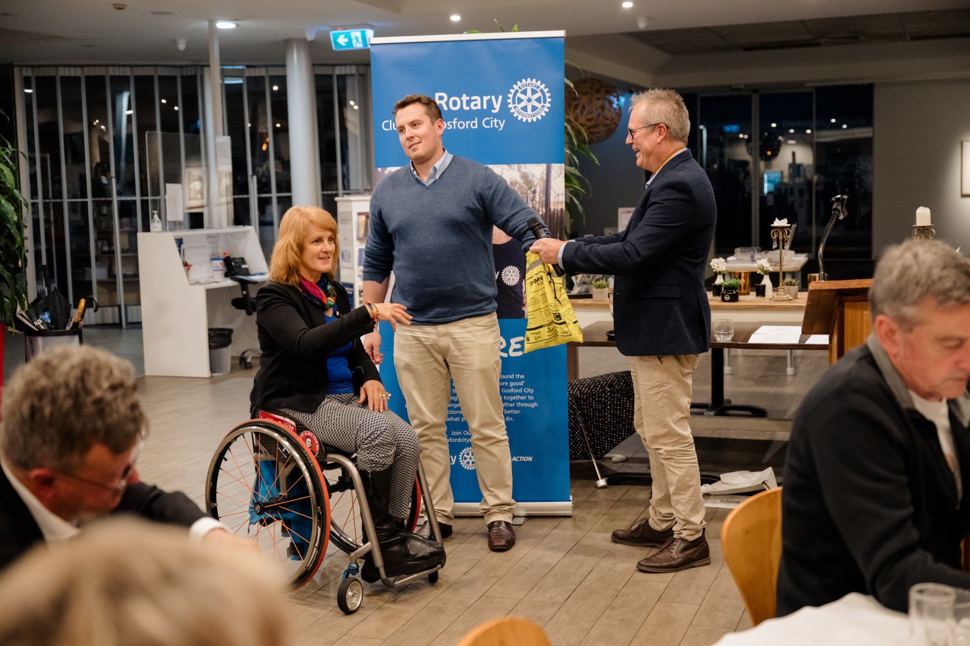 A woman in a wheelchair is receiving a gift from a man in a suit.