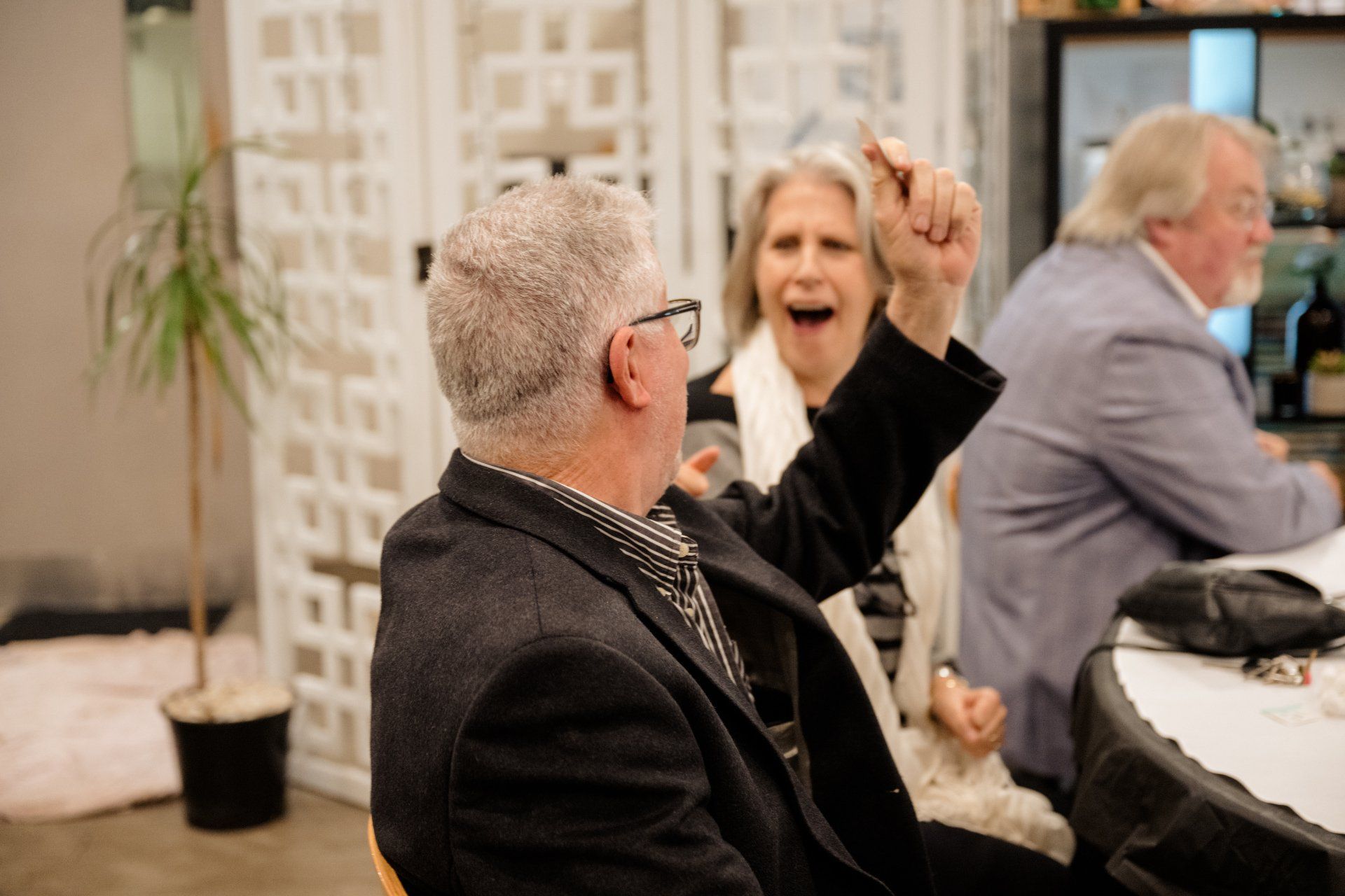 A man and a woman are sitting at a table with their hands in the air.