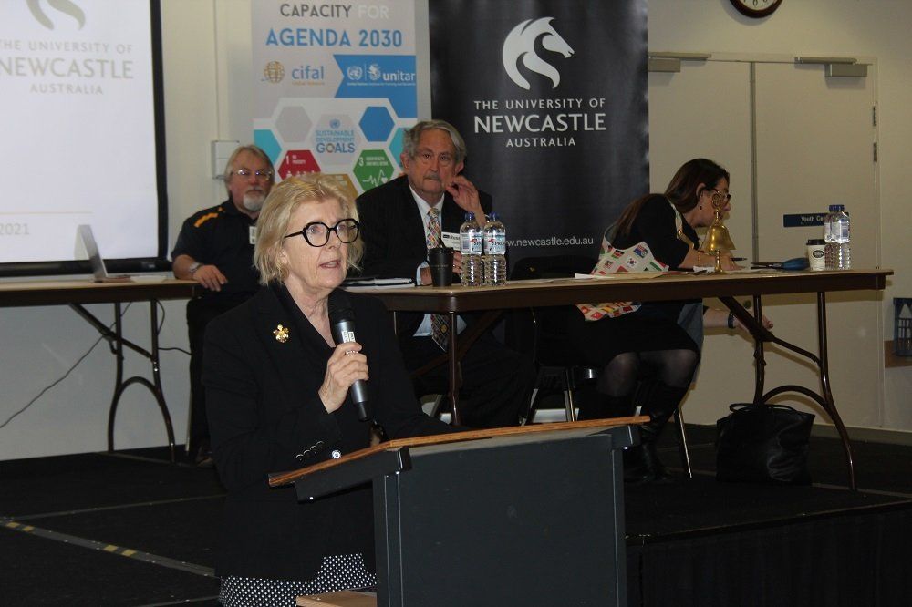 A woman is giving a speech in front of a newcastle banner