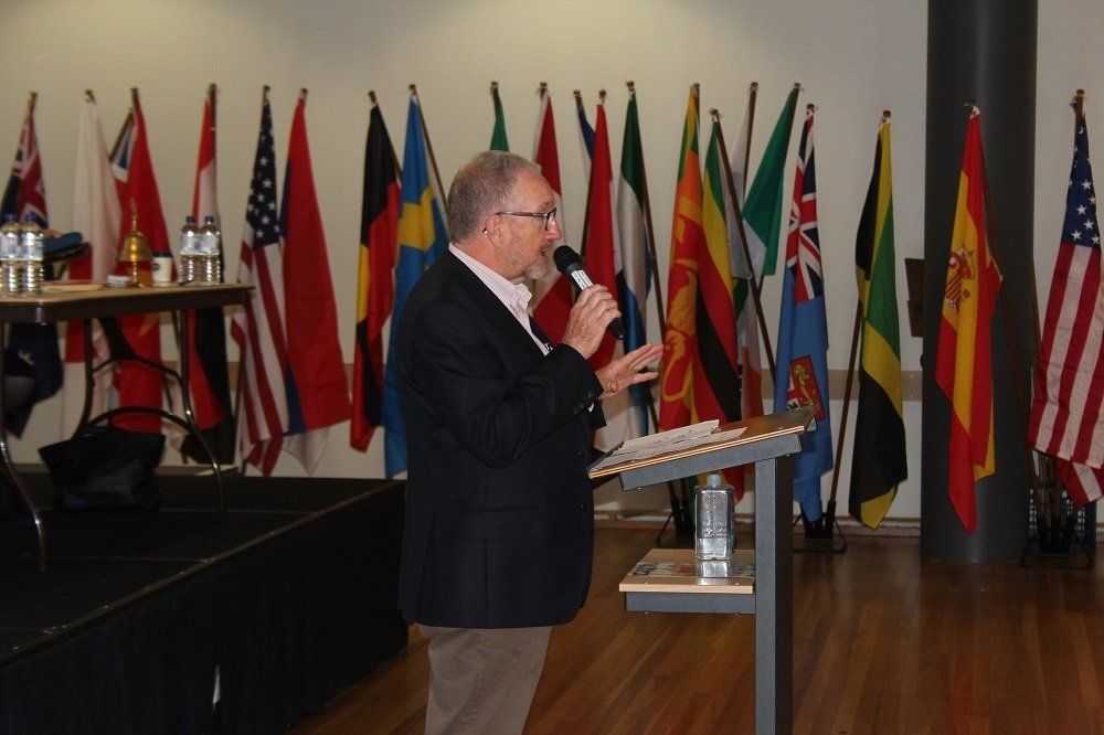 A man speaking into a microphone in front of a row of flags