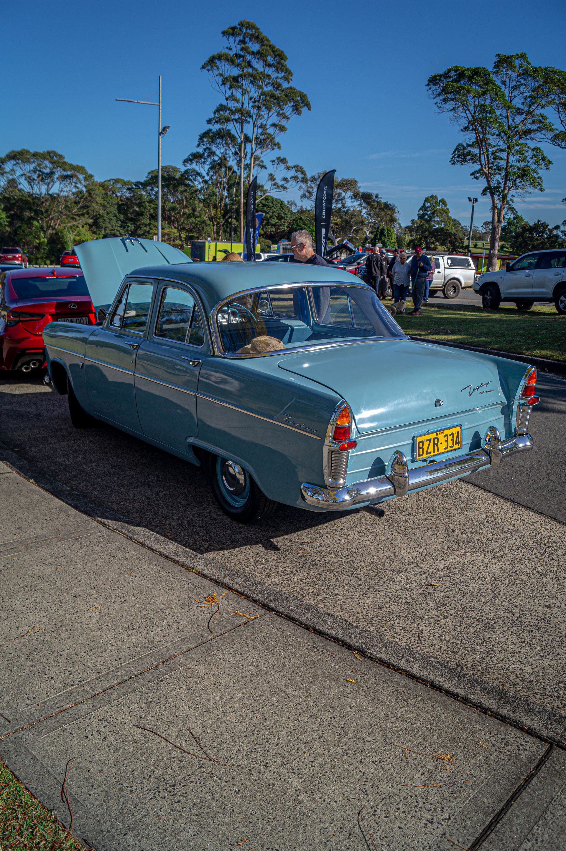 A blue car with the hood up is parked on the side of the road.