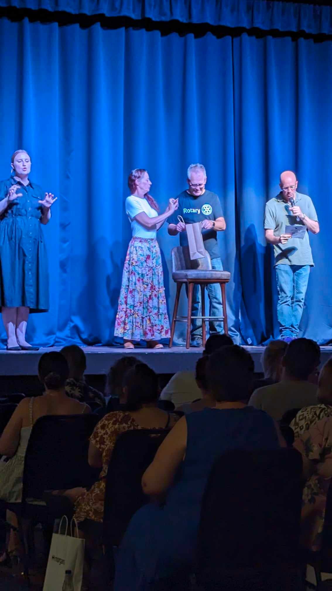 A group of people are standing on a stage in front of a blue curtain.