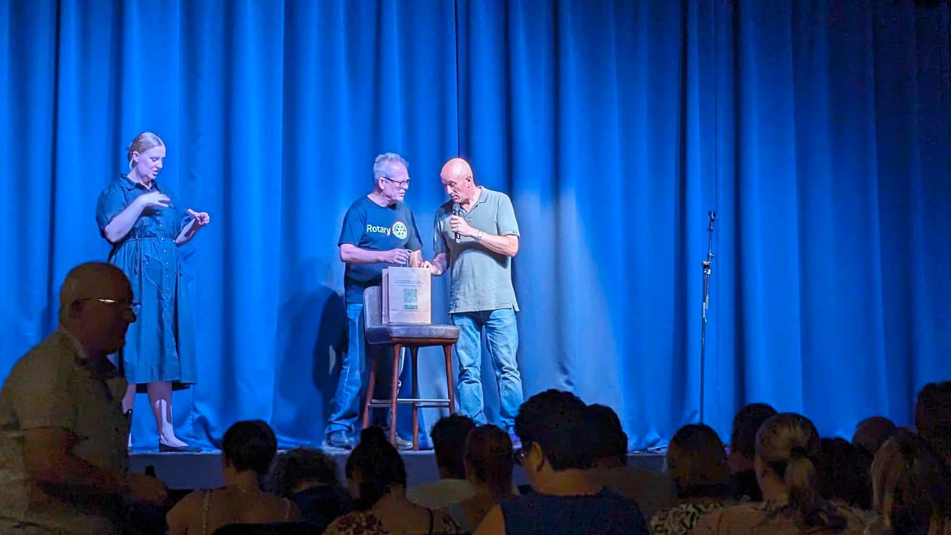 A group of people are standing on a stage in front of a blue curtain.