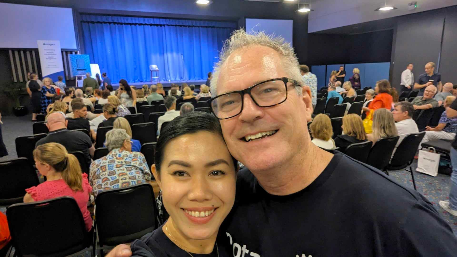 A man and a woman are posing for a picture in front of a crowd.
