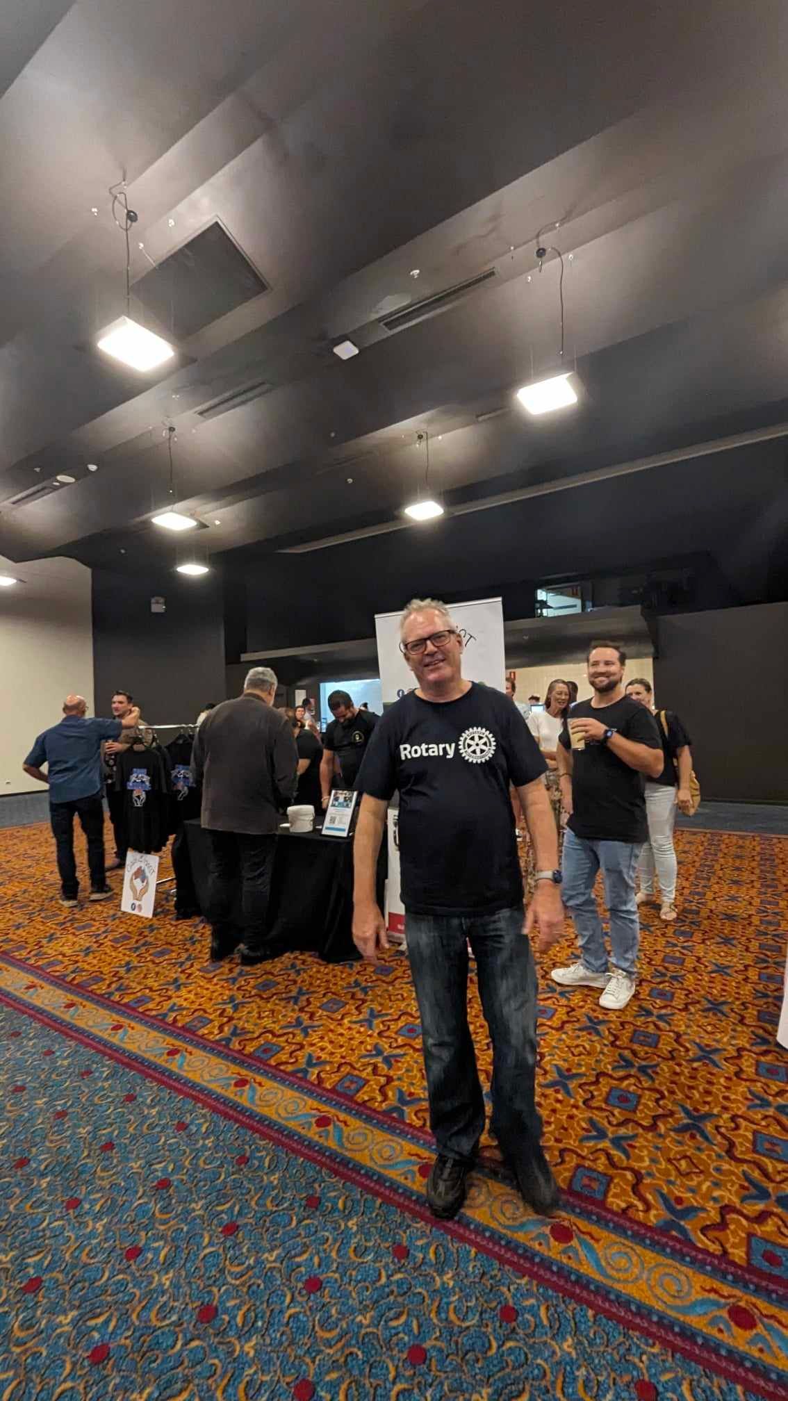 A man is standing in a large room with a group of people.