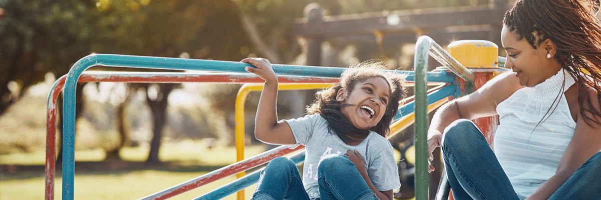 Children laughing on colorful playground equipment outdoors in warm sunlight