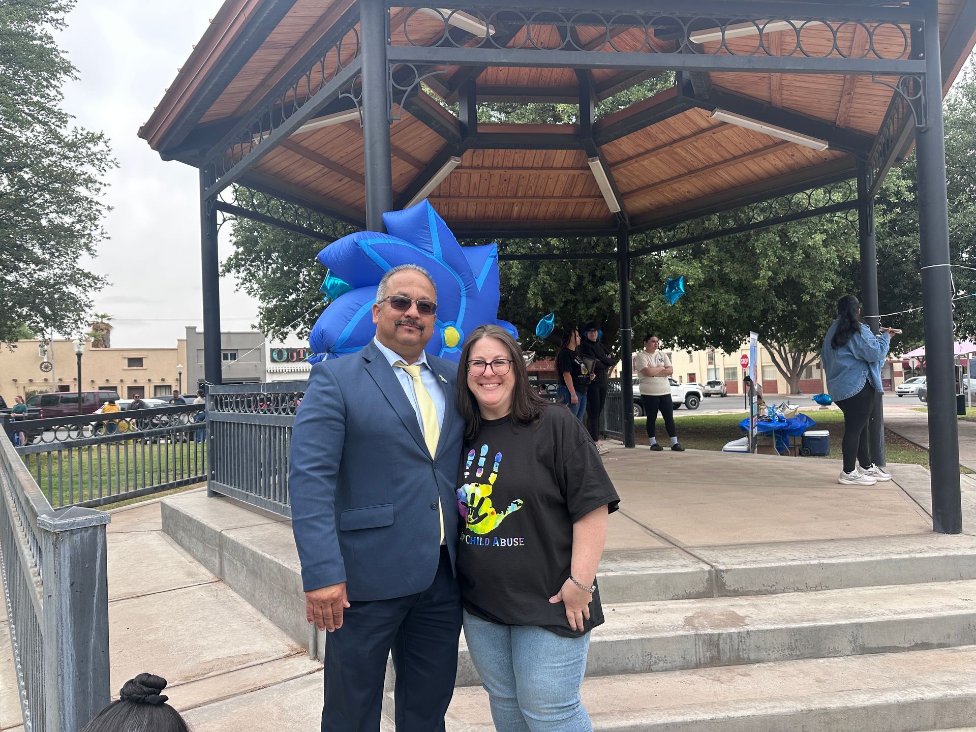 Two people posing under a pavilion beside a large blue balloon decoration.