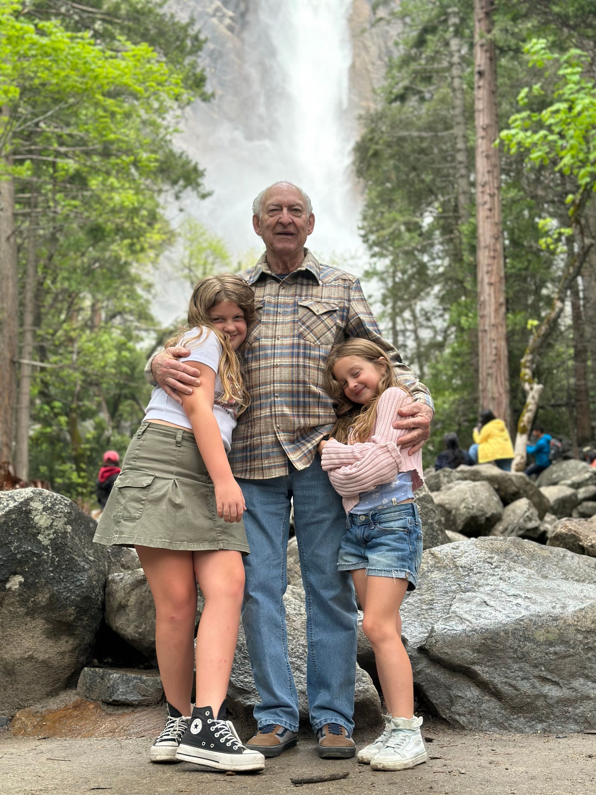 A man and two girls are standing in front of a waterfall.