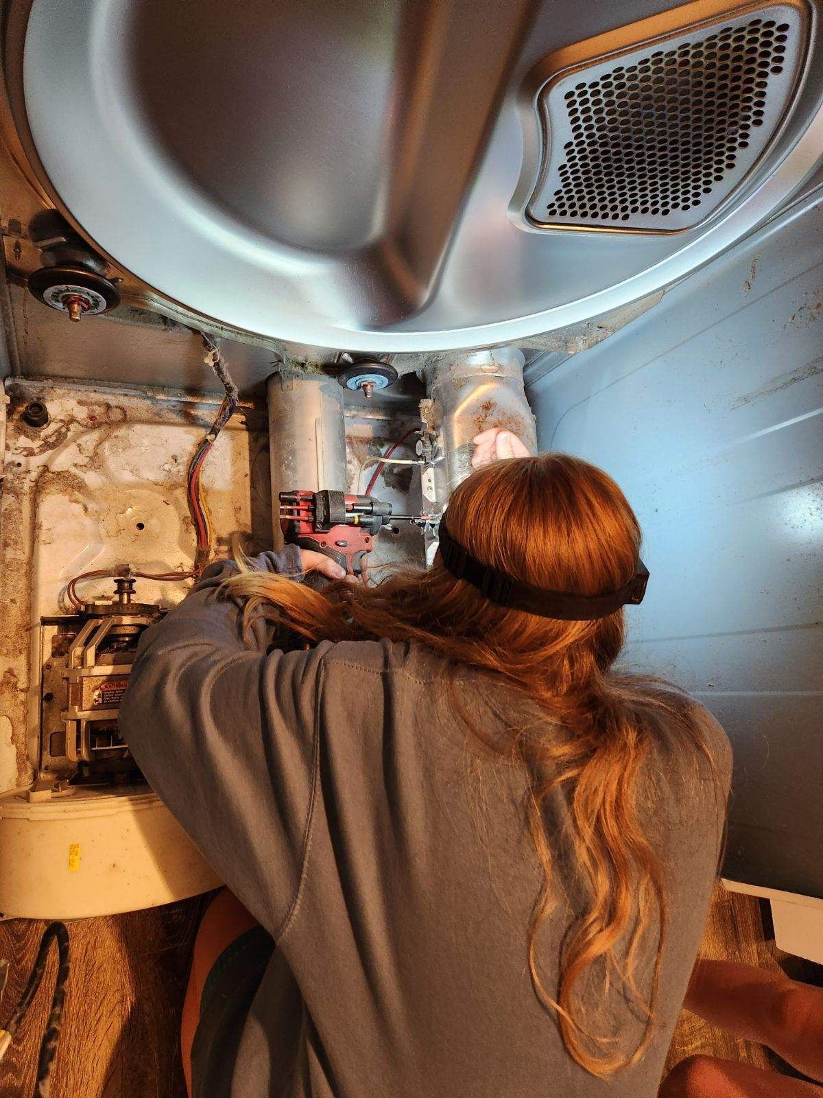 A woman is working on a dryer with a drill.