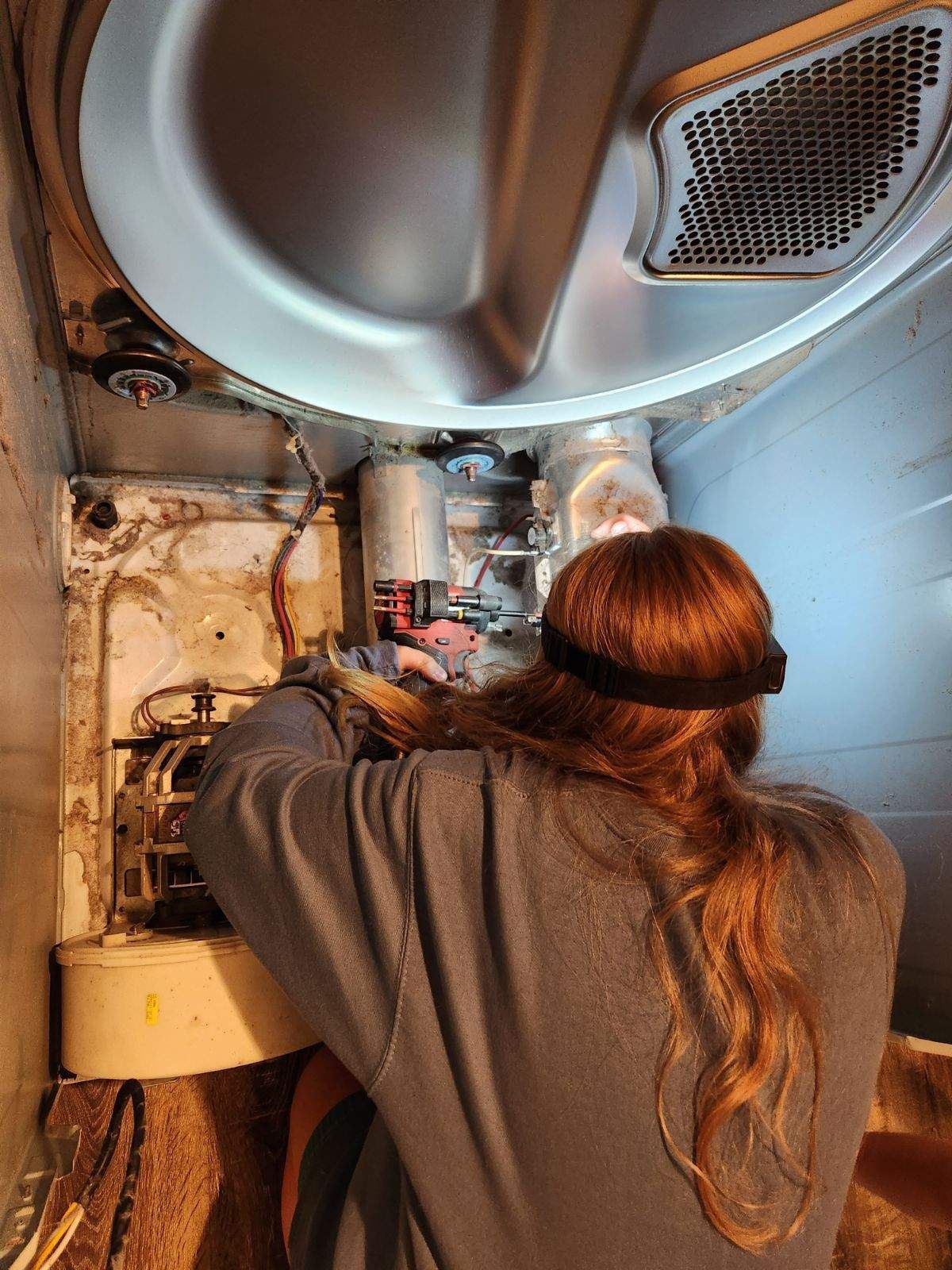 A woman is working on a washing machine in a bathroom.