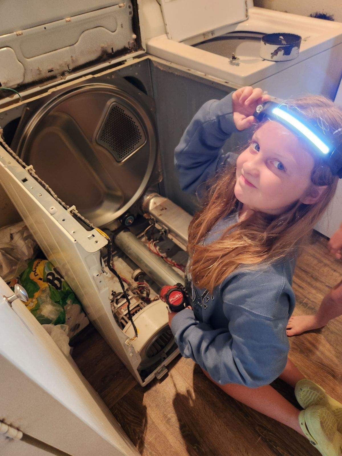 A little girl is sitting on the floor next to a washing machine and dryer.