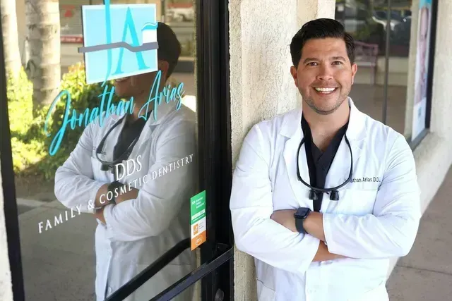 A man in a lab coat is standing in front of a dental office.