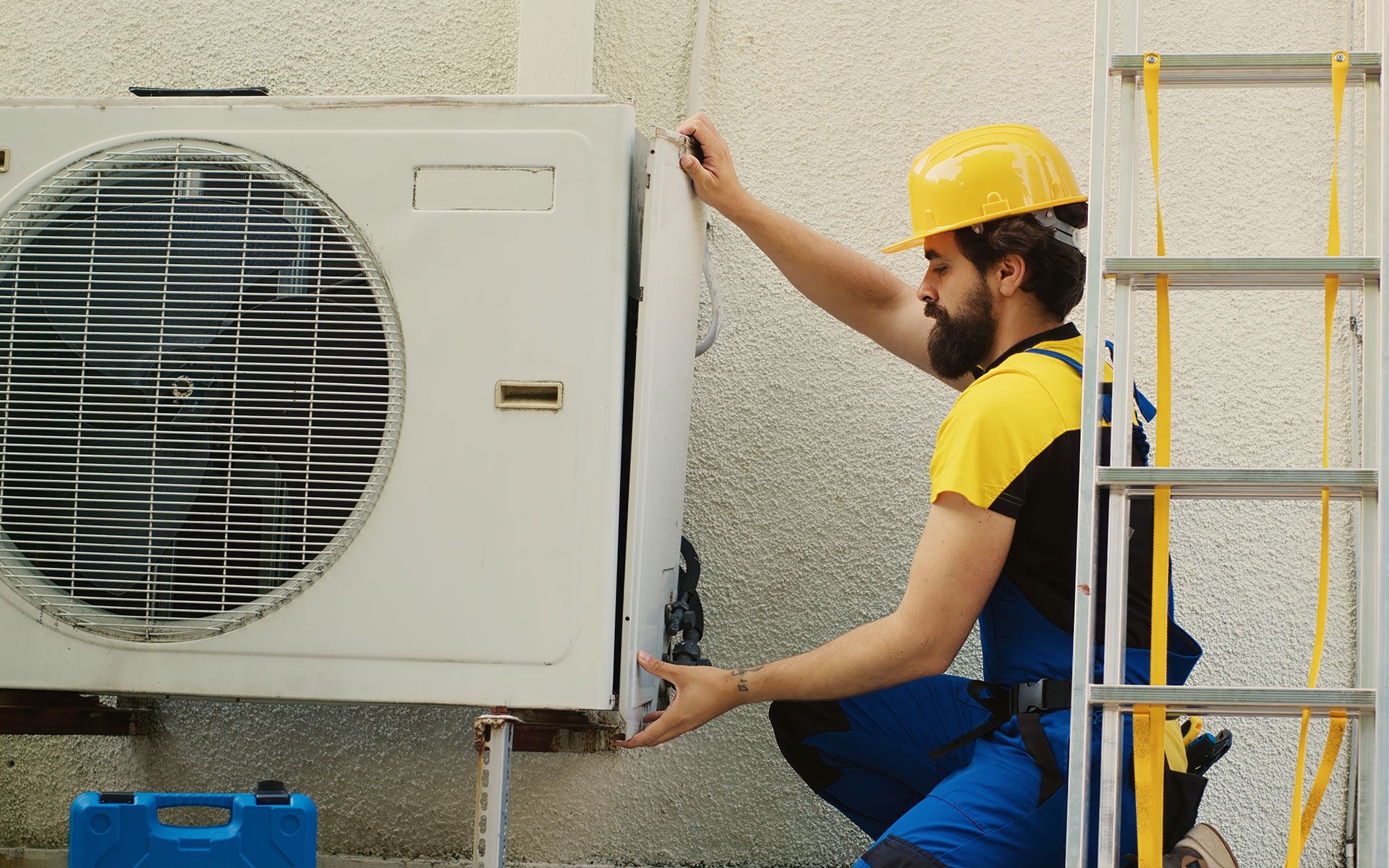 A man is kneeling down next to a ladder fixing an air conditioner.