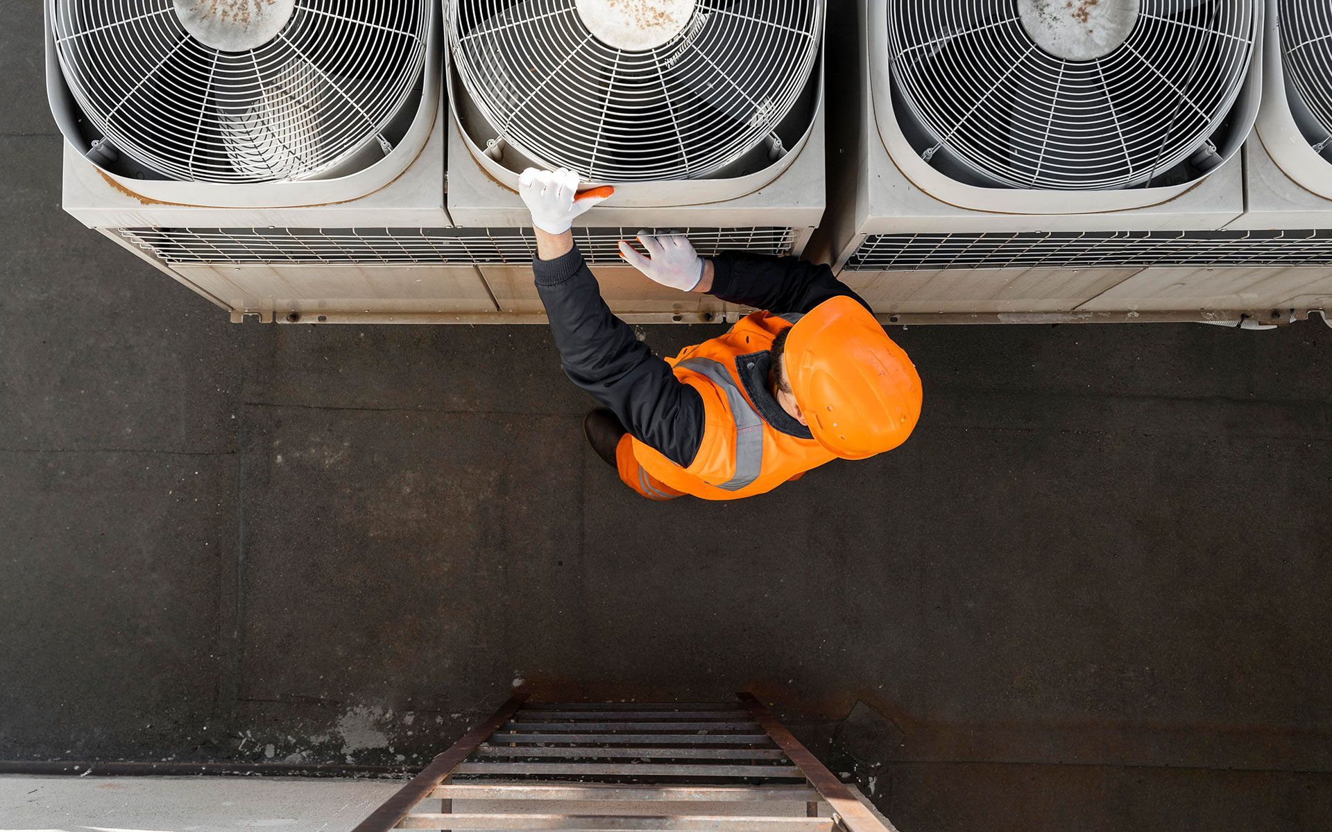 A man is standing on a ladder working on an air conditioner.