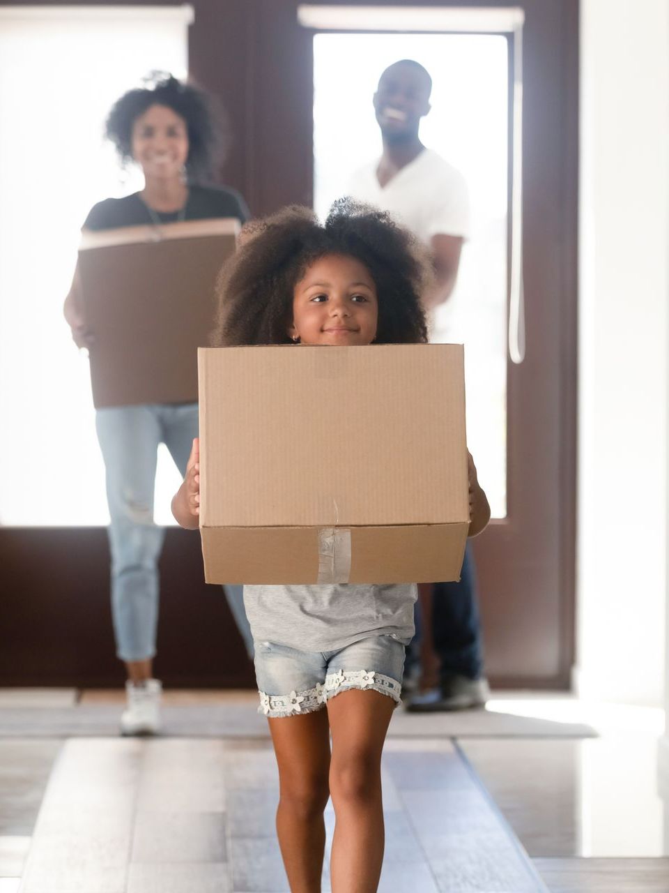 A little girl is carrying a cardboard box in front of her parents.